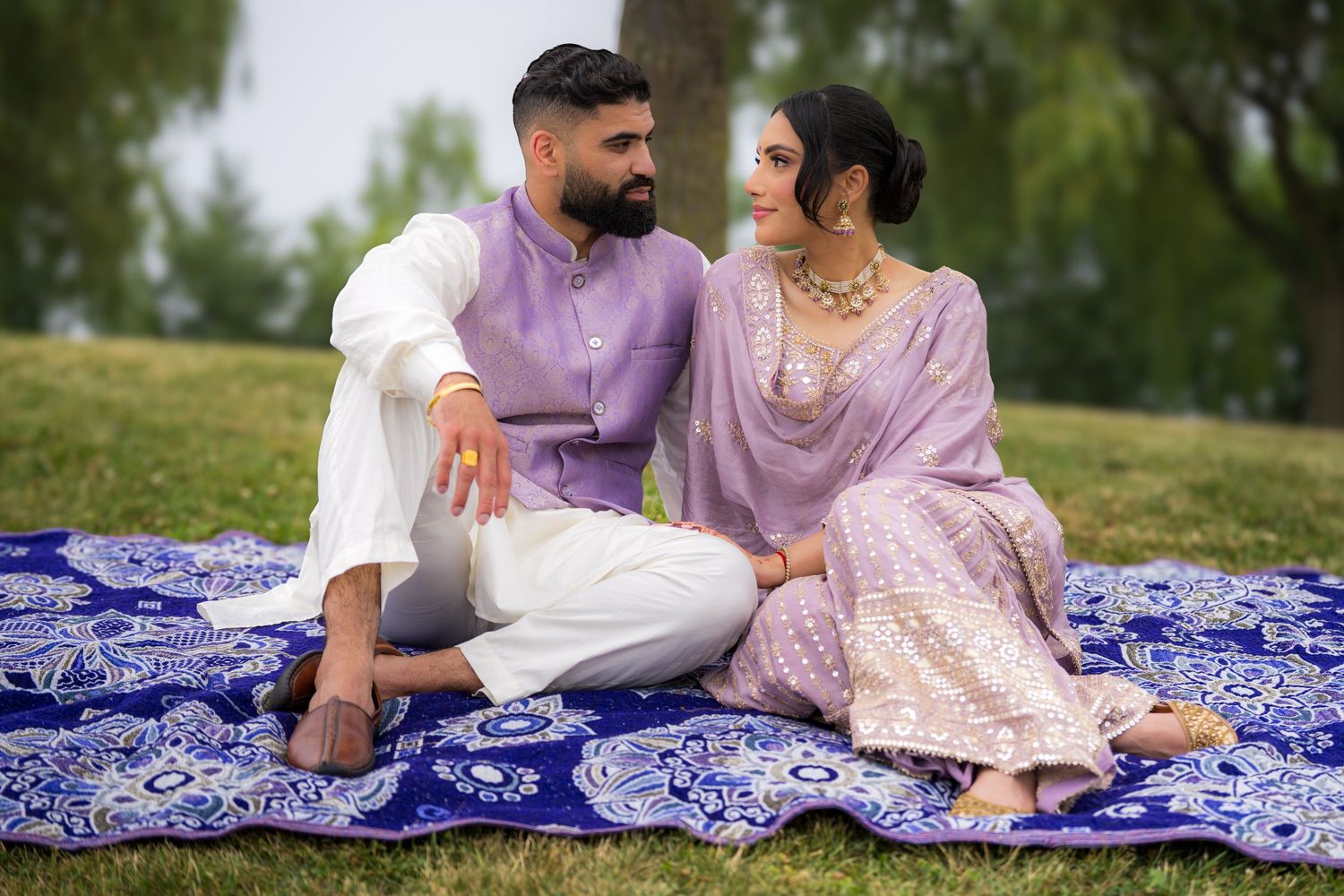Couple lounging on decorative blue blanket during outdoor engagement session in park setting.