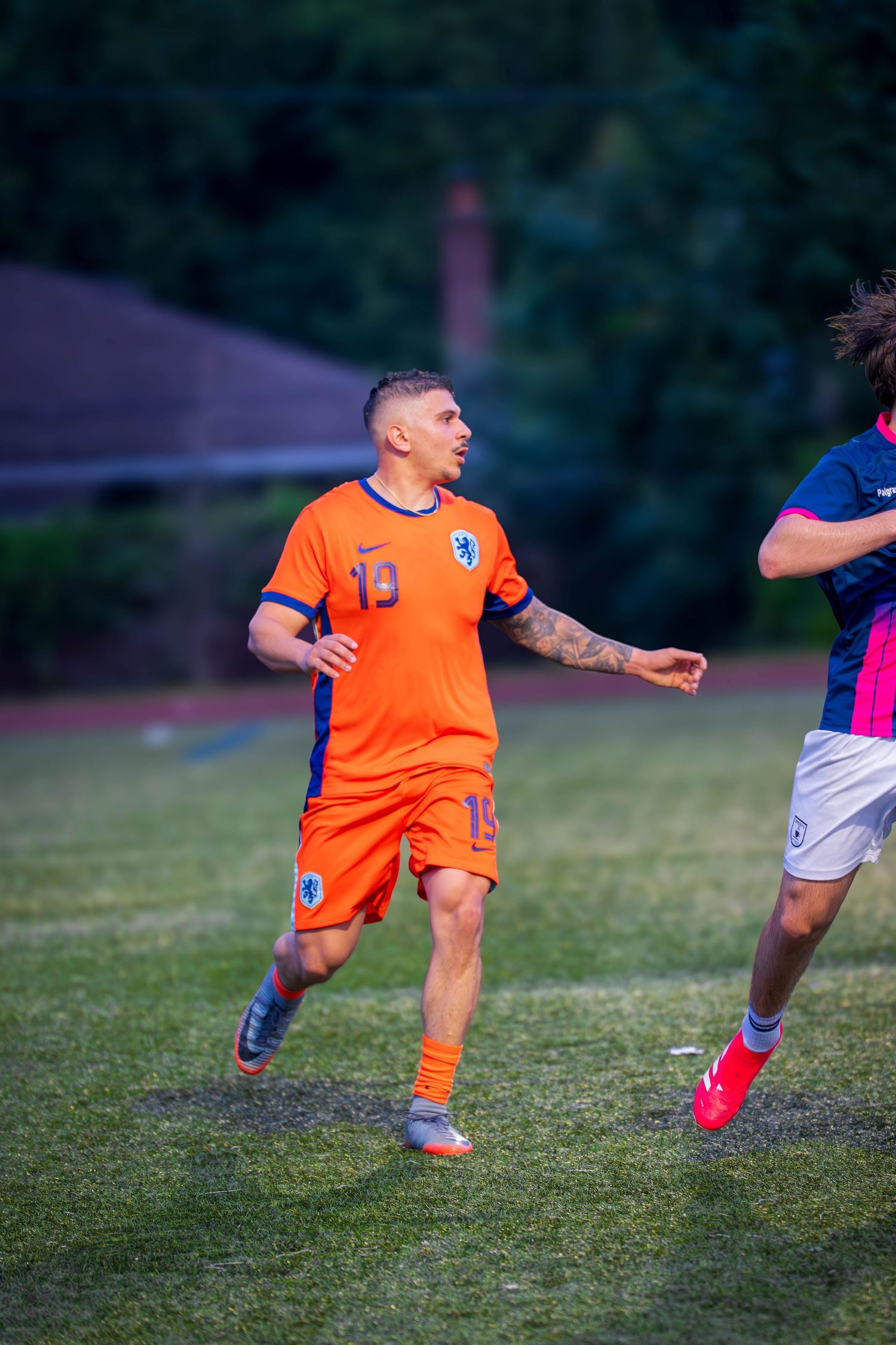 Soccer player in vibrant orange uniform moves across field during evening game.