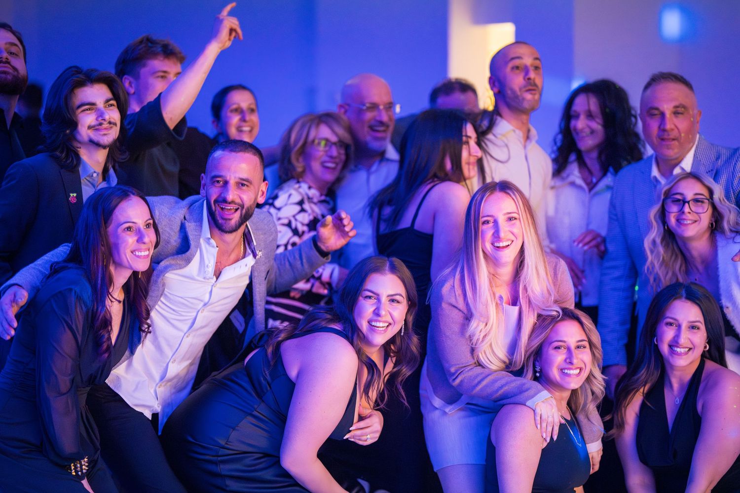 Crowd of party guests dancing and celebrating under blue event lighting.