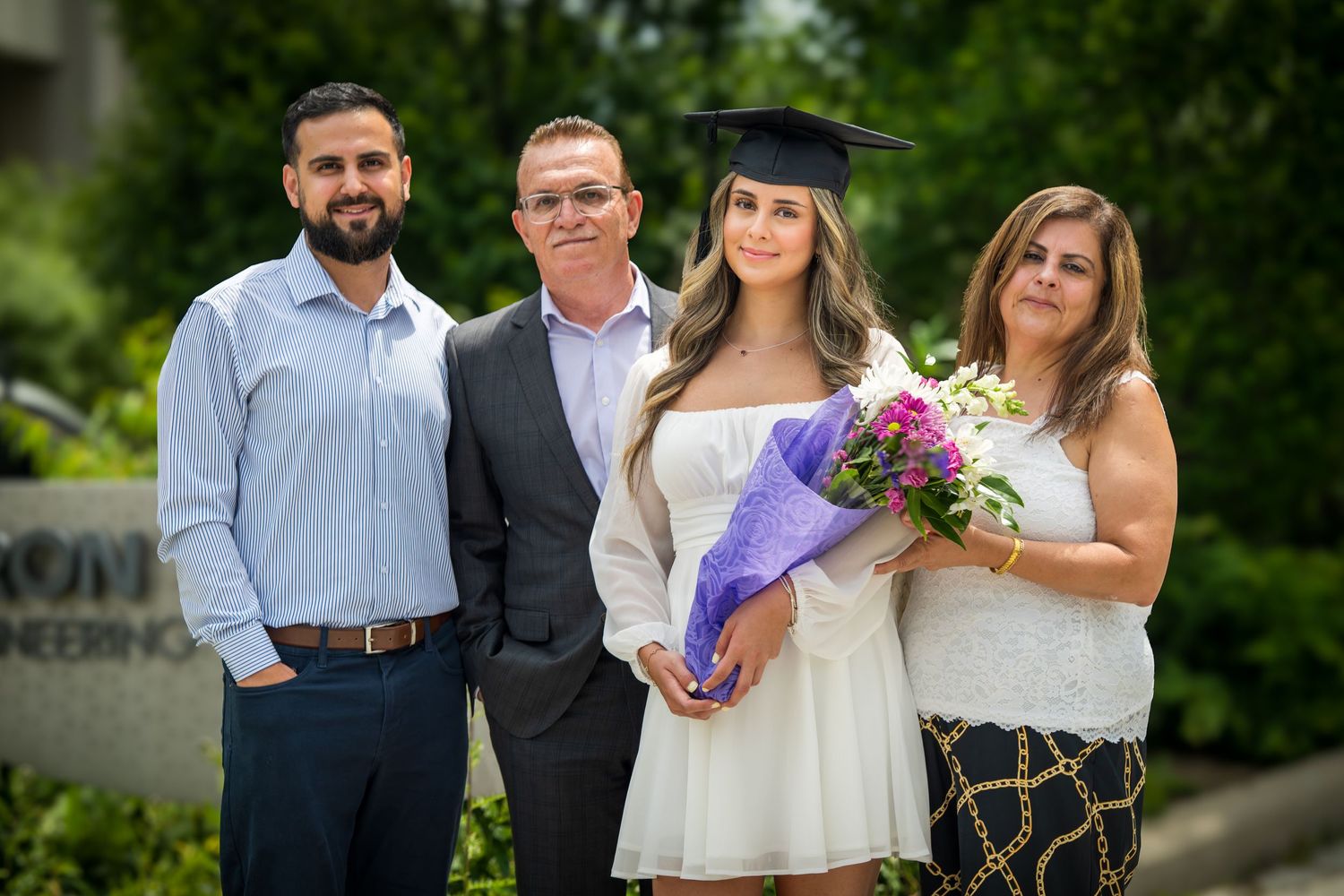 Group photo taken outdoors with greenery in background showing graduation celebration.