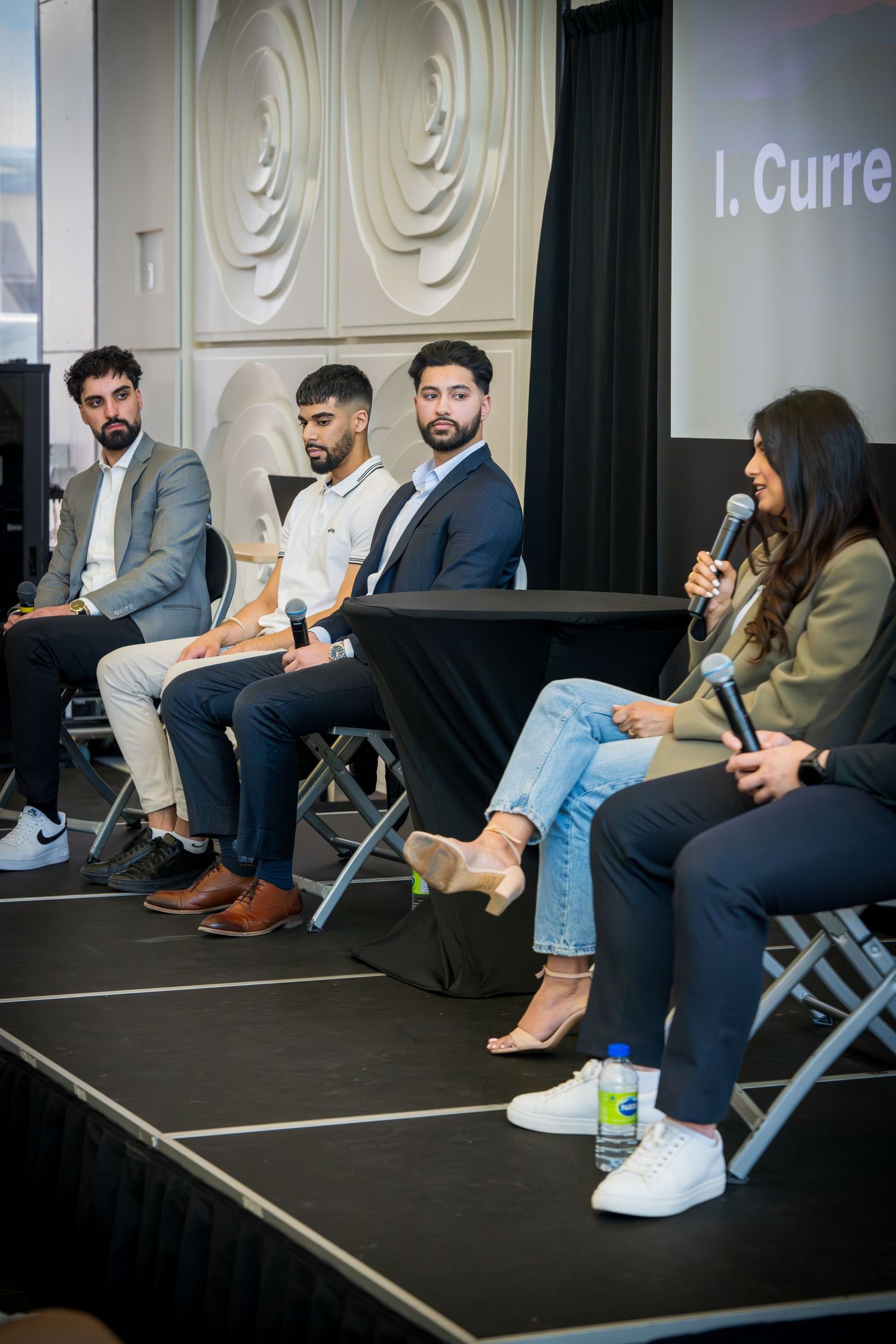 Side view of panelists sitting on stage showing diverse business attire and casual footwear.