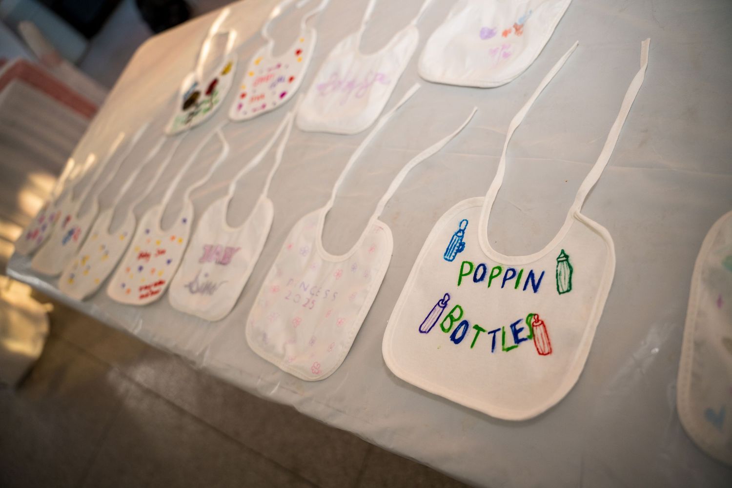 Decorated white baby bibs displayed in a row with hand-drawn designs and names.