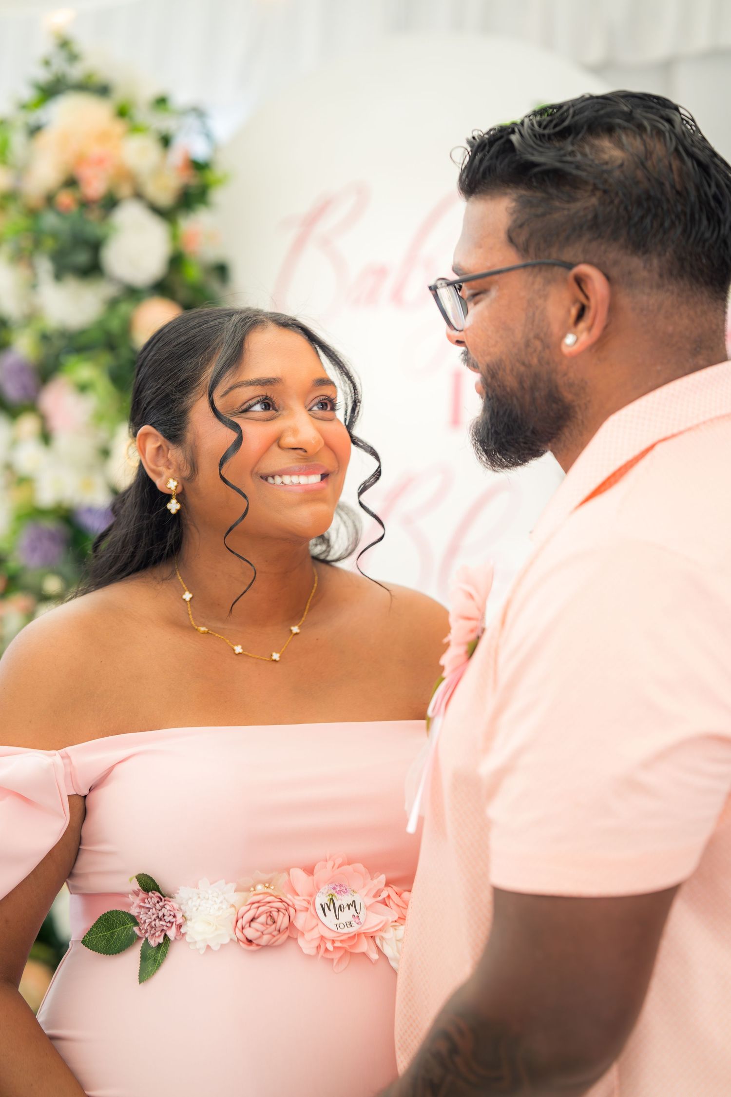 A couple poses intimately against a backdrop of pink and peach flowers at a celebration.