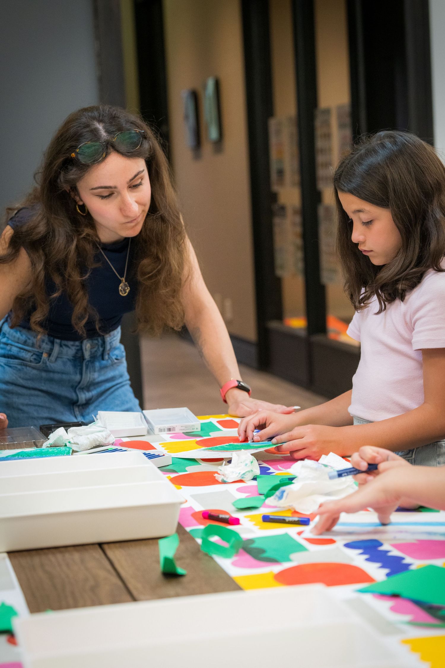 Woman and girl working together on a vibrant collage art project with colorful paper pieces.