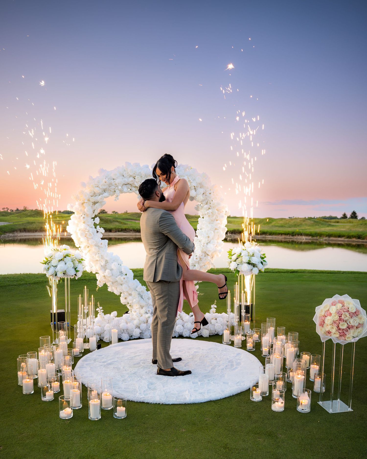 Elegant proposal scene with white flower arch and glowing candles at dusk.