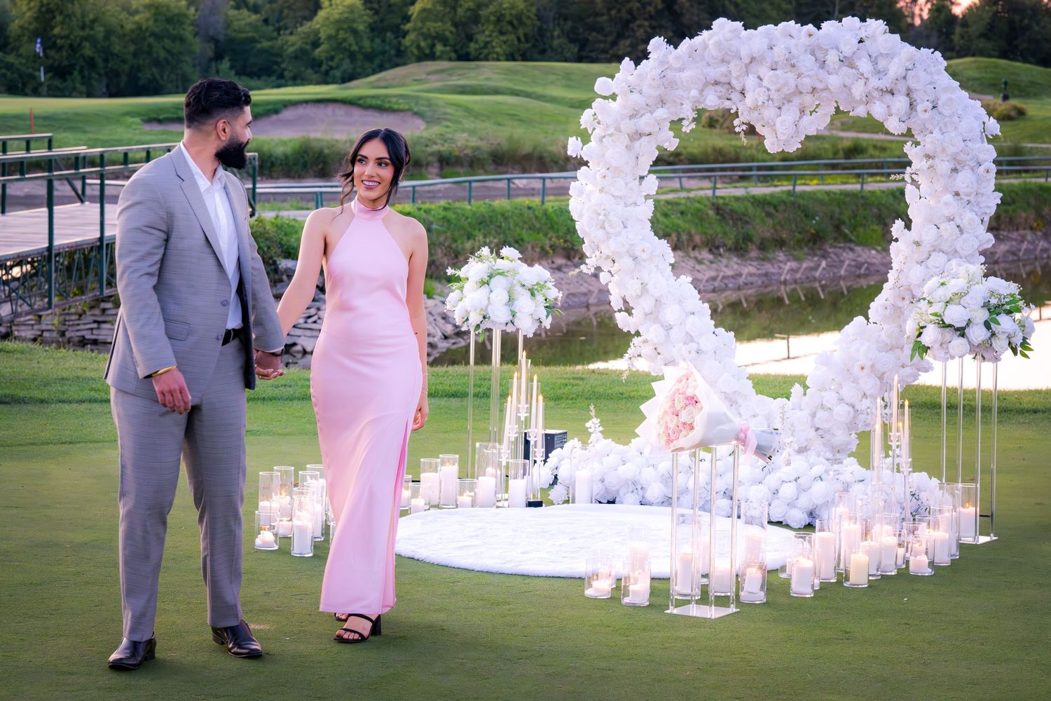 Wedding ceremony site decorated with white balloon arch and candles on a golf course.