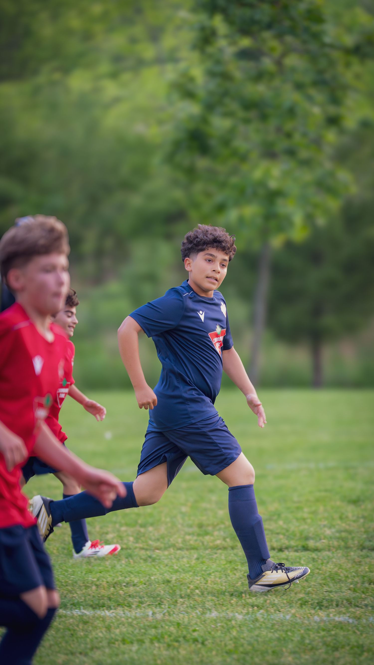 Soccer players in red and blue uniforms run across a grass field during a match.