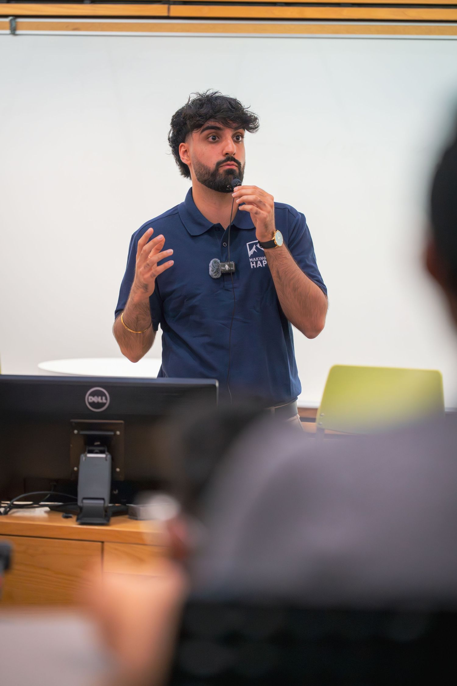 Speaker in navy blue polo shirt gesturing animatedly during a presentation.