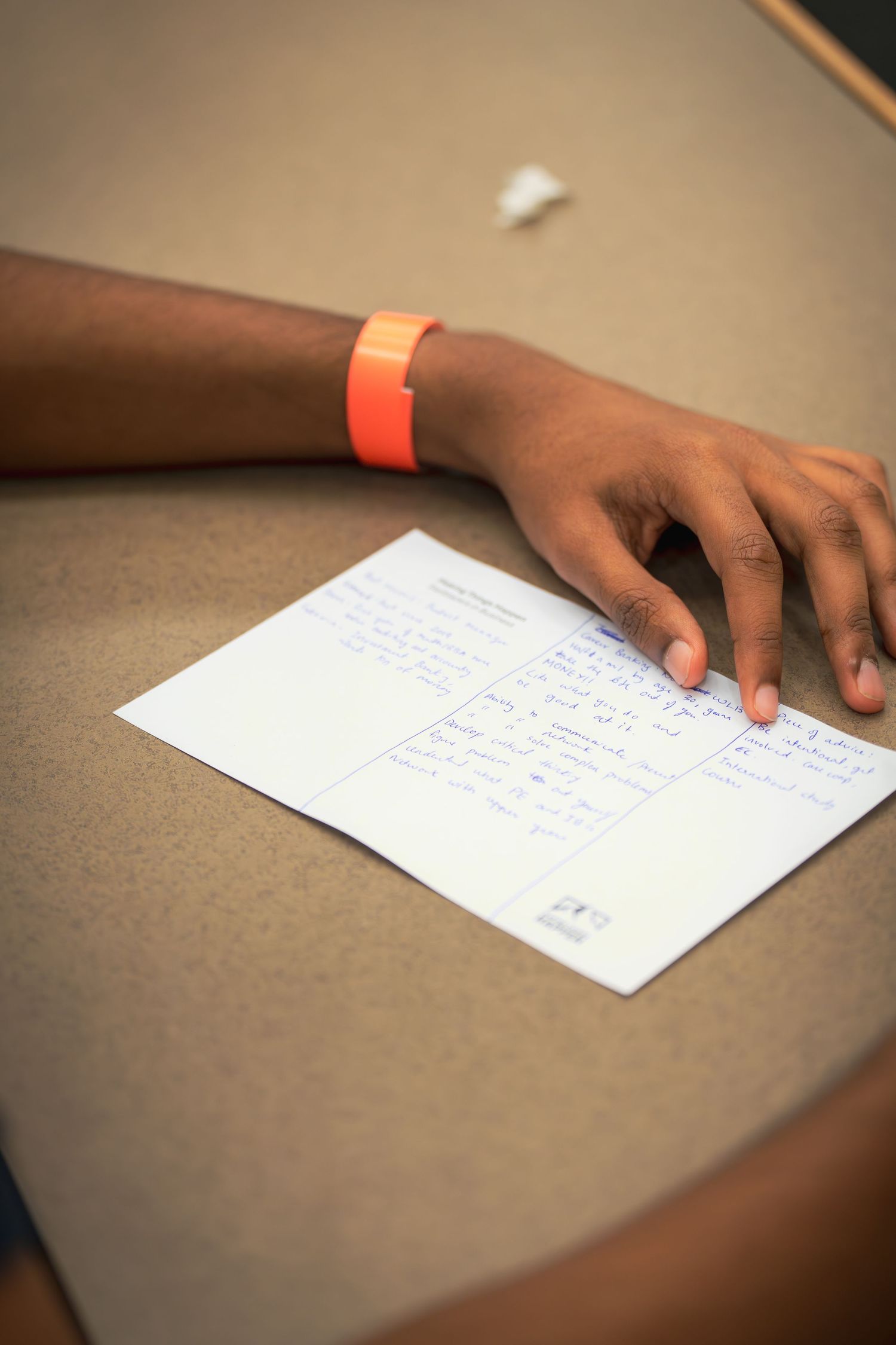 Close-up of hands with orange wristband reviewing written notes on paper.