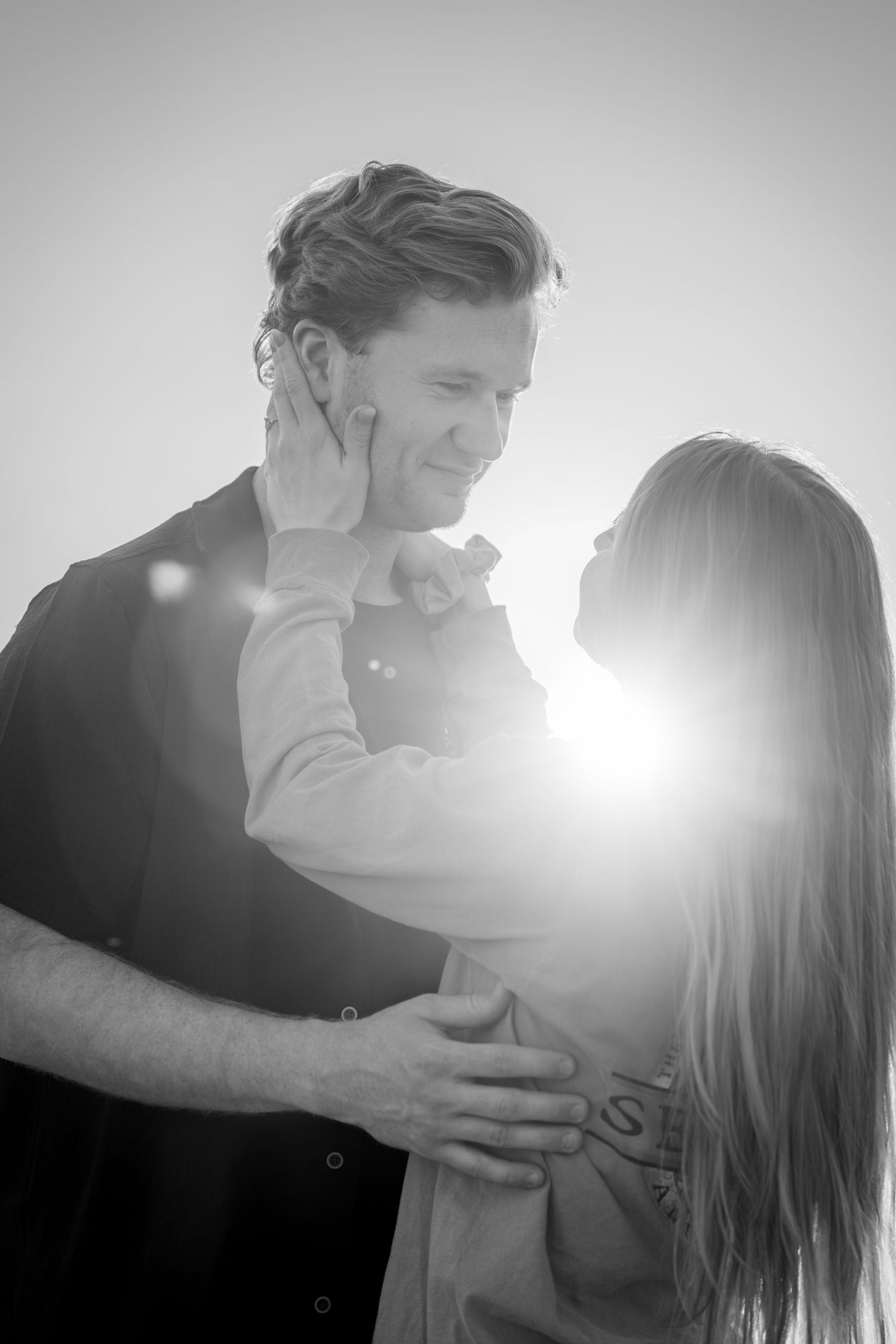 Black and white photo of a couple embracing tenderly with bright sunlight creating a glowing backdrop.