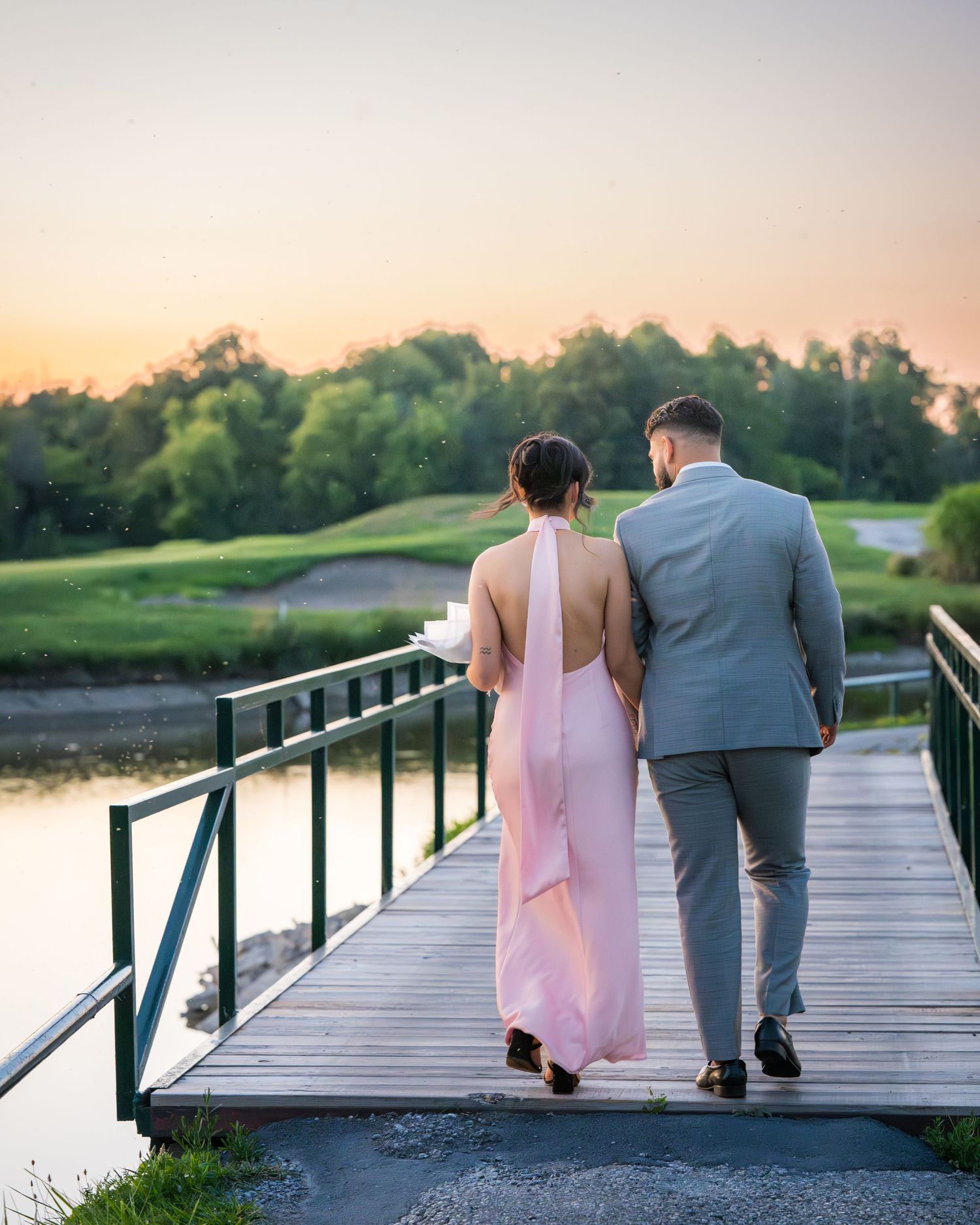 Two people walking along a lakeside boardwalk during a peaceful sunset.
