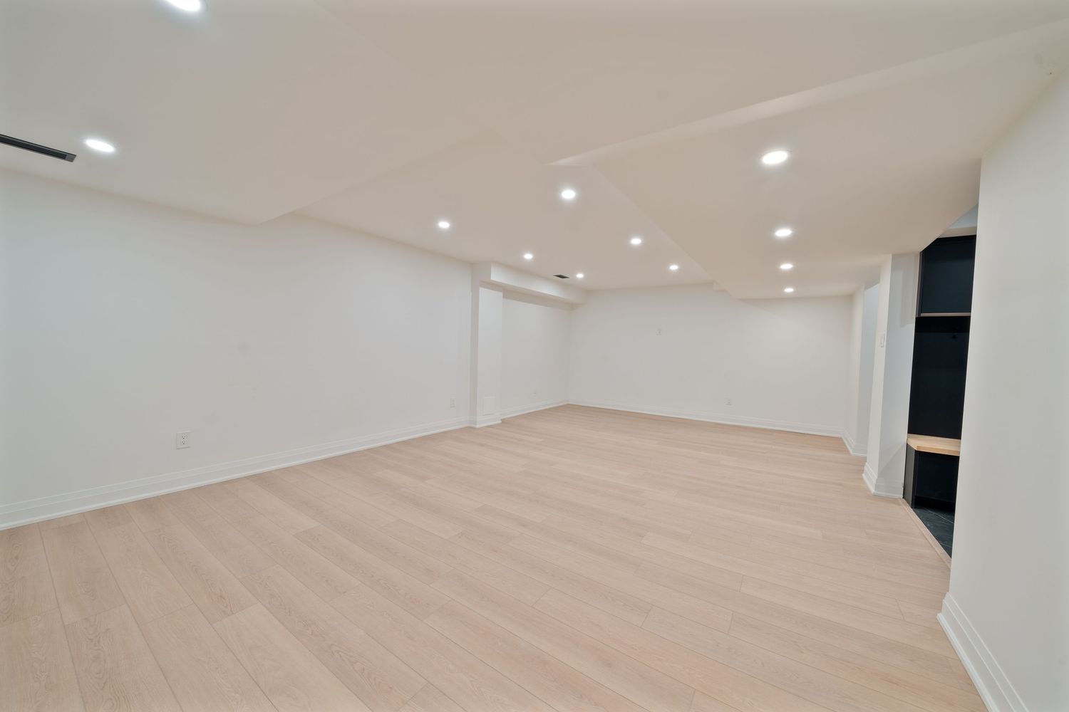 Modern white room interior with recessed lighting and light wood flooring stretches along a minimalist hallway.