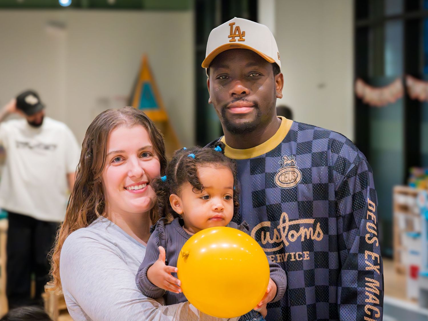 Happy interracial family posing together with their young daughter holding a yellow balloon at an indoor event.