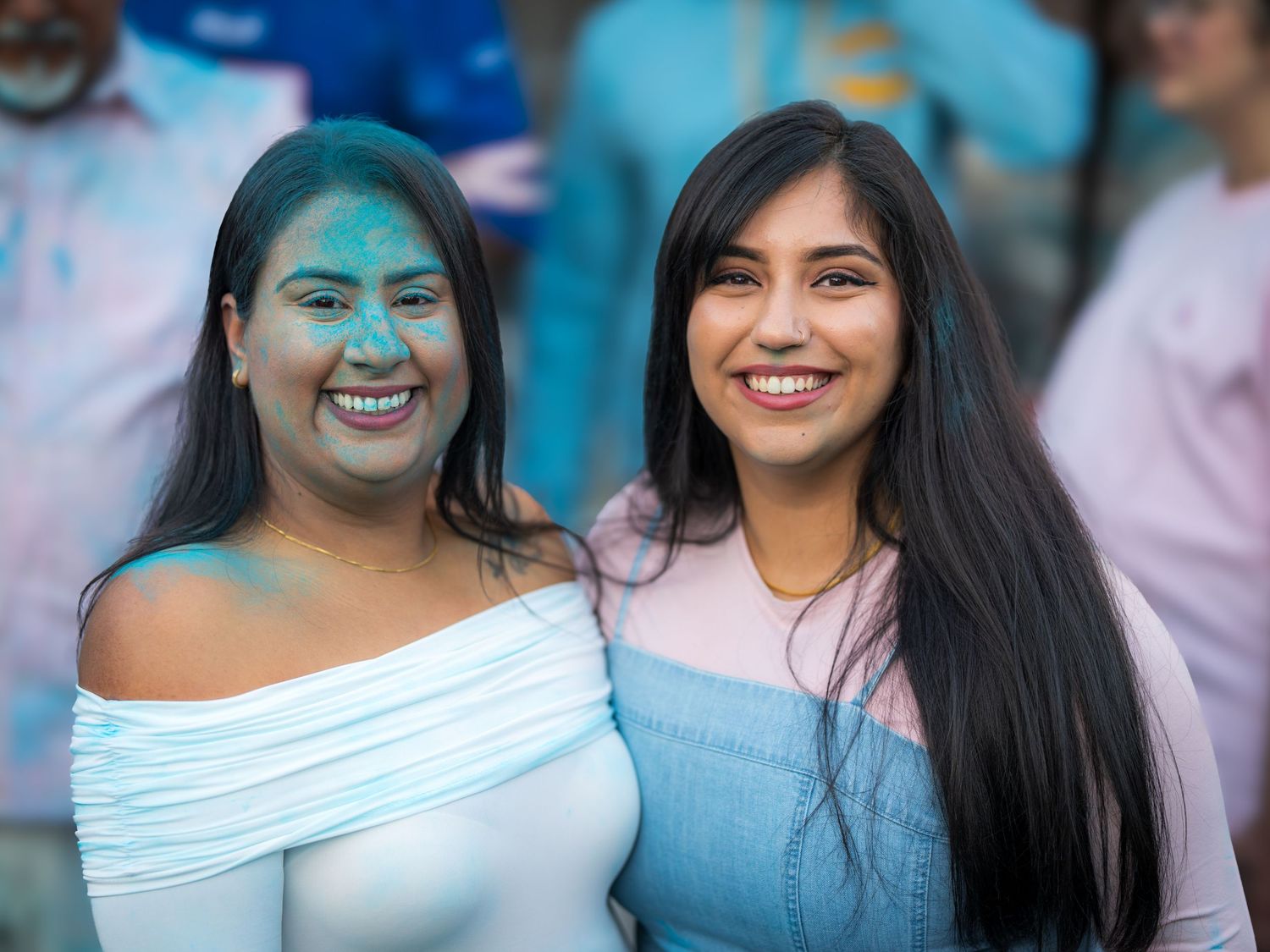 Two smiling women, one with blue powder on face, pose at a gender reveal celebration.