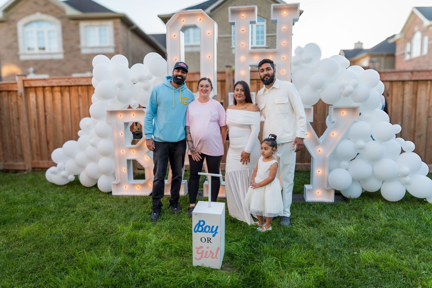Family posing at outdoor gender reveal party with Boy or Girl box and illuminated BABY letter backdrop.