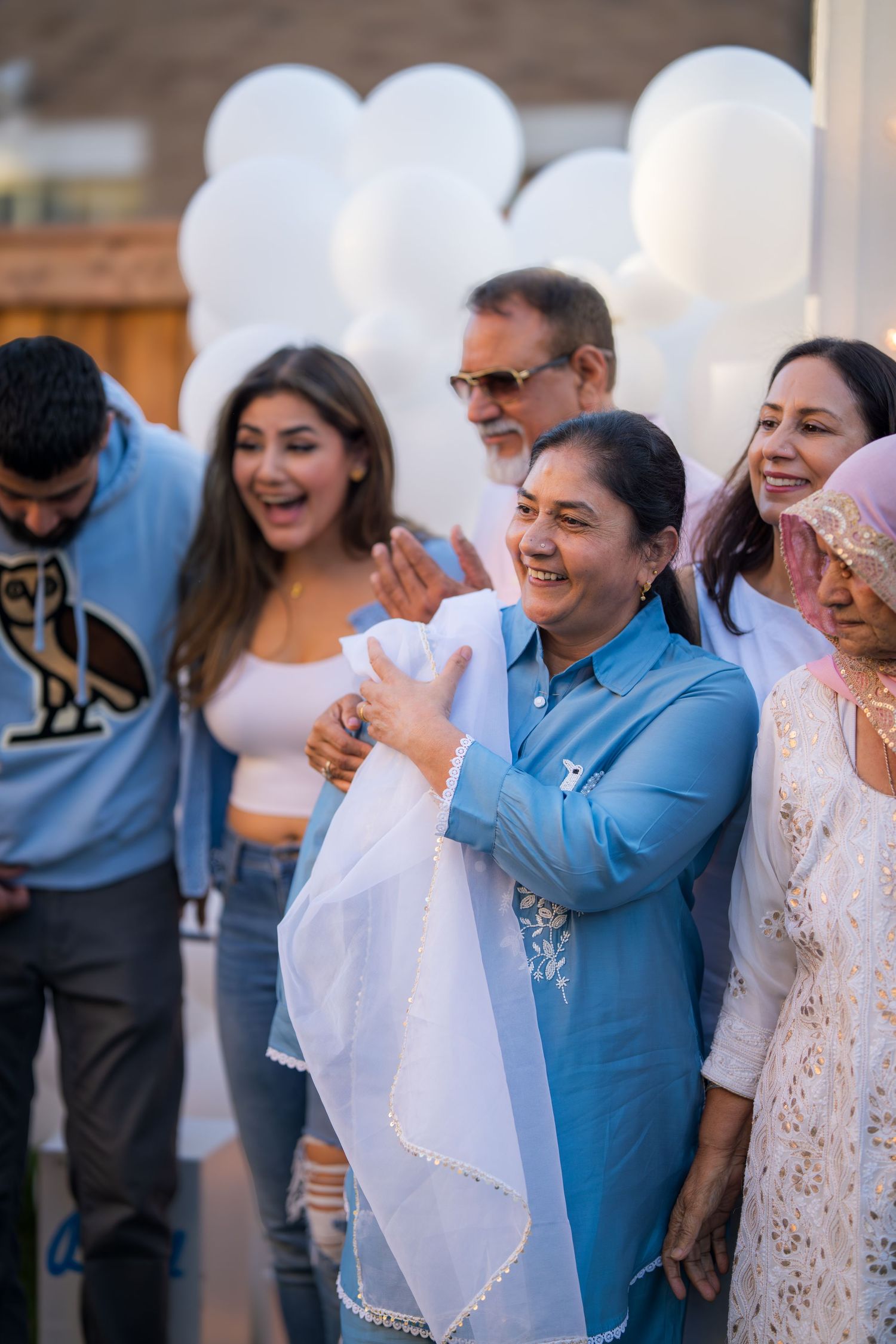 Family members laugh and celebrate together at an outdoor gender reveal party with white balloons.