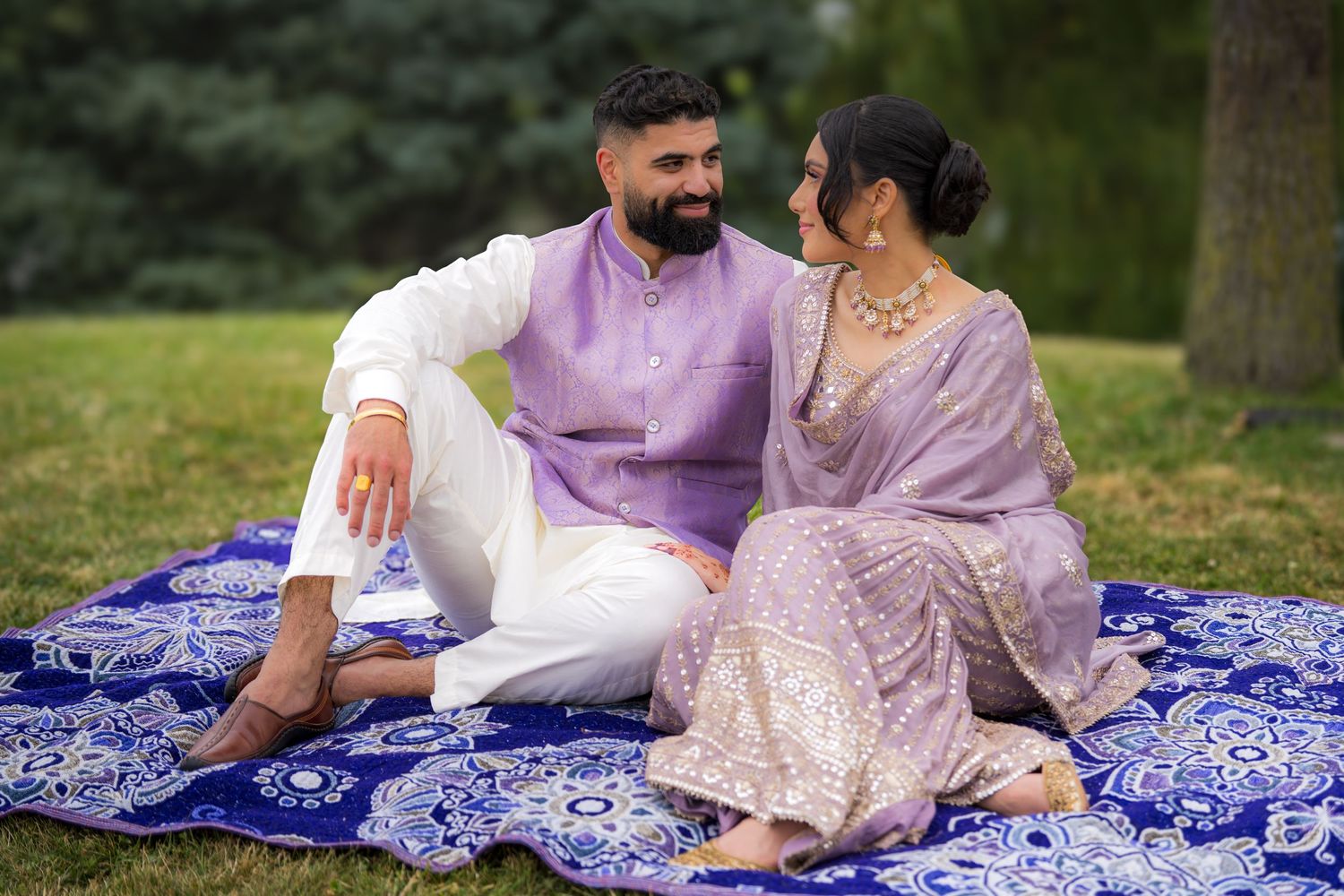 Romantic couple poses on blue patterned blanket during outdoor garden photography session.