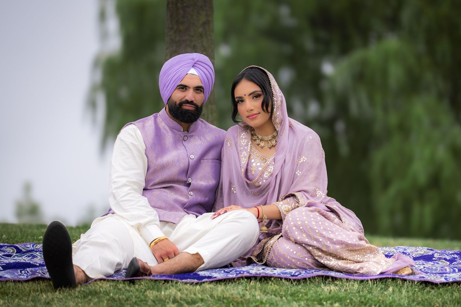 A couple in lavender and white outfits sitting together on a blue blanket in a park setting.