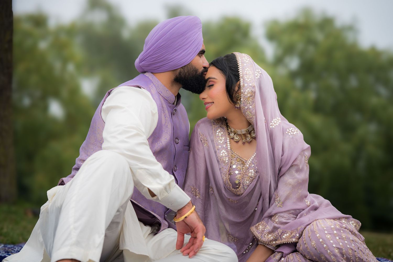 Couple shares tender moments in matching lavender and white traditional wedding outfits.