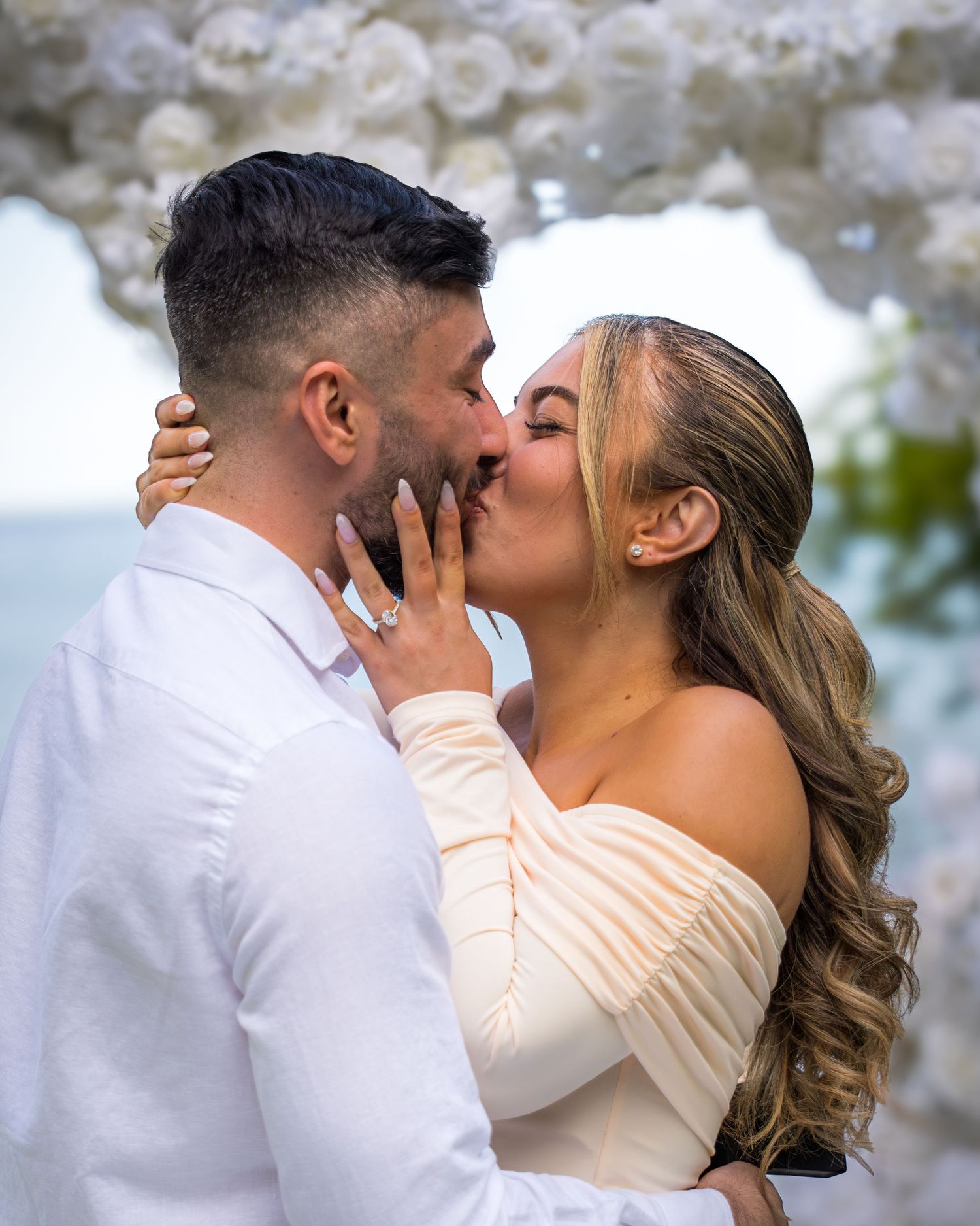 Romantic kiss captured under white balloon arch decorations.