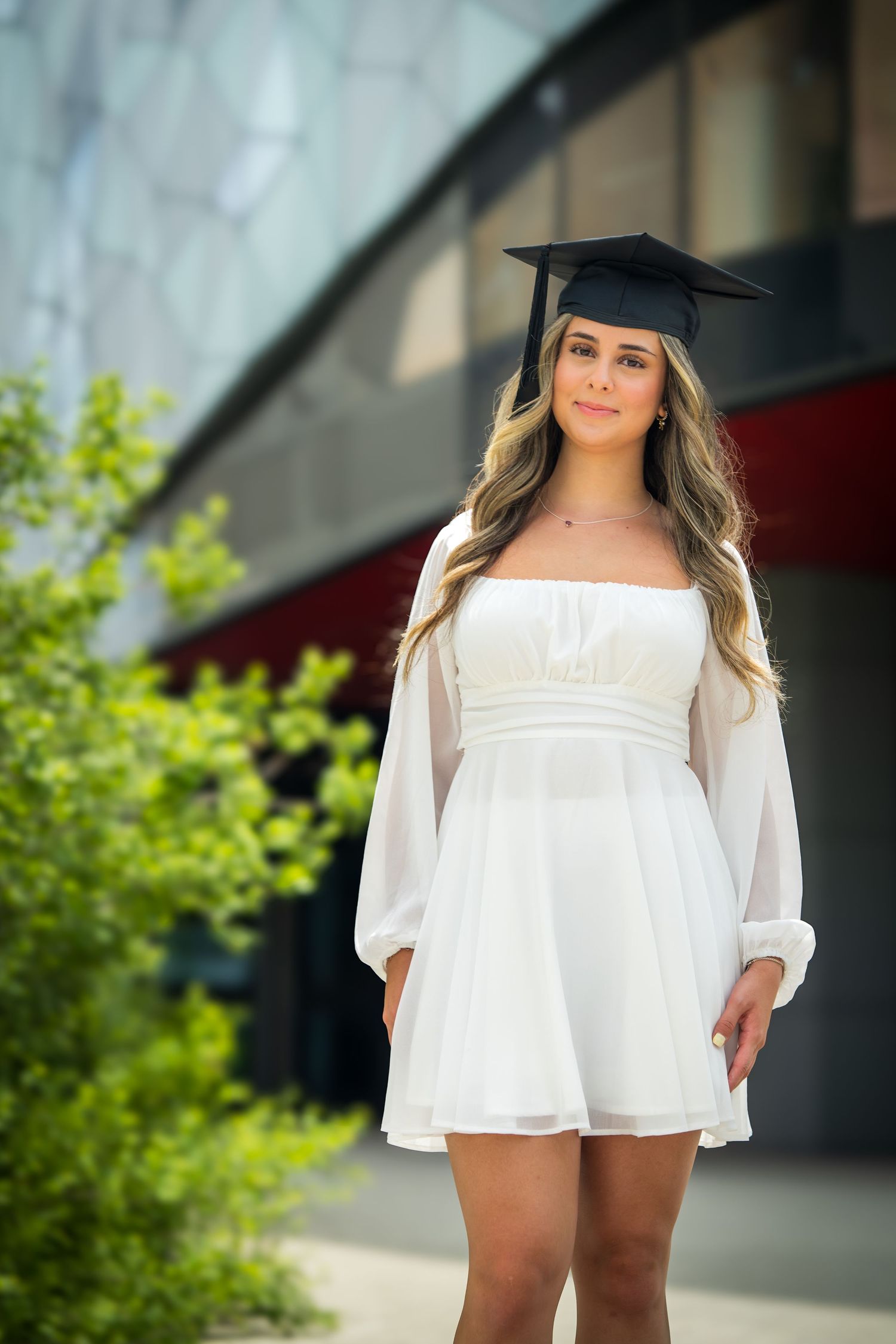 Graduate poses in flowy white dress during outdoor photo session.