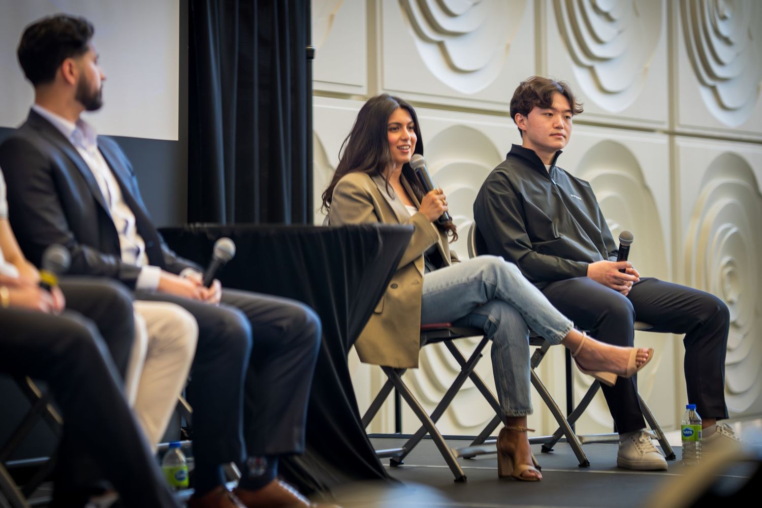 Side angle view of panel discussion with speakers seated against decorative wall backdrop.