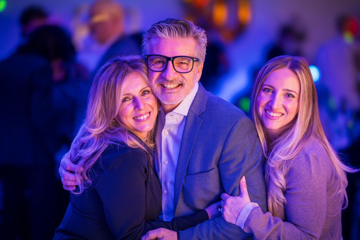 Group of people smiling and celebrating together under colorful party lighting.