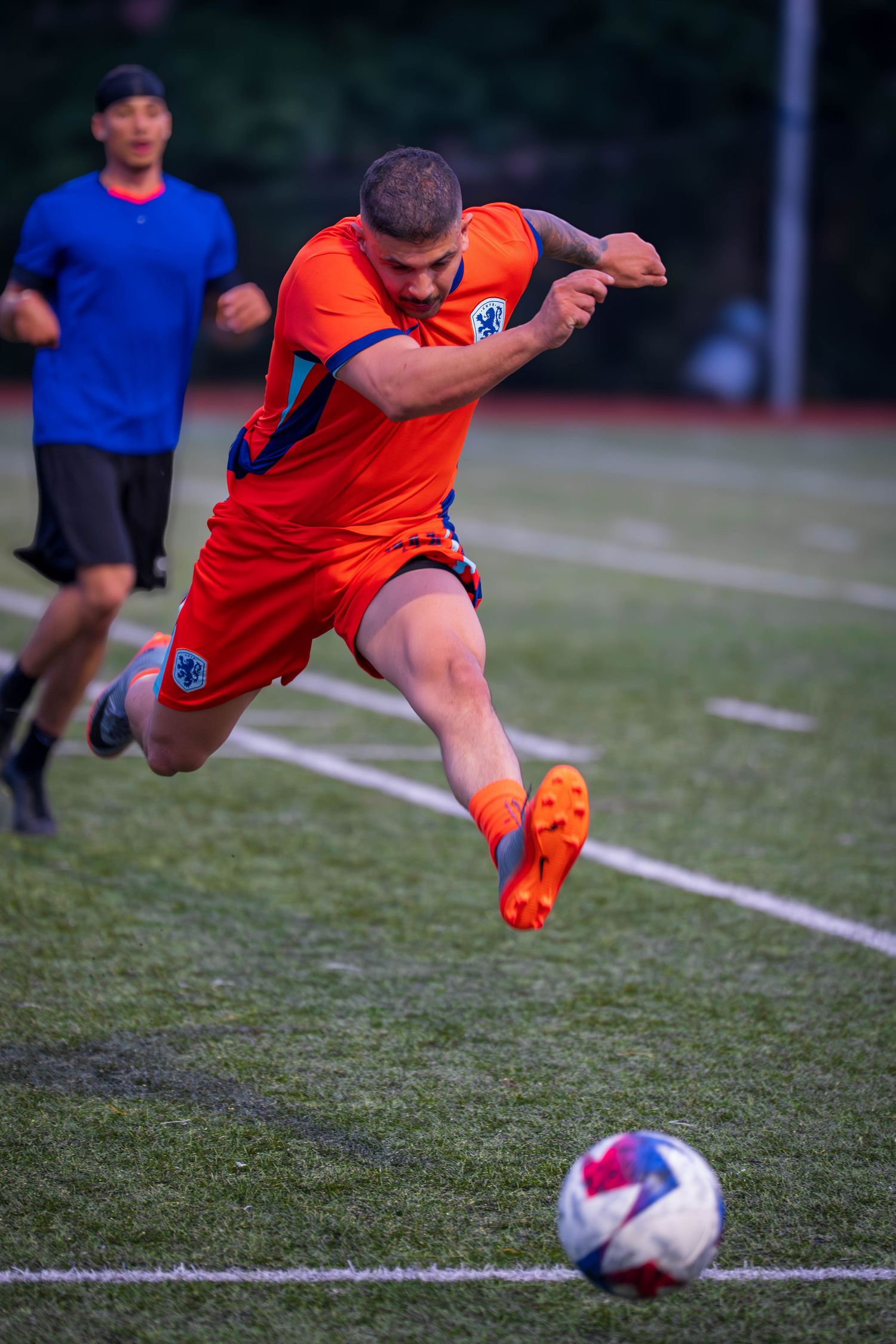 Soccer player in orange uniform executes powerful kick during match.