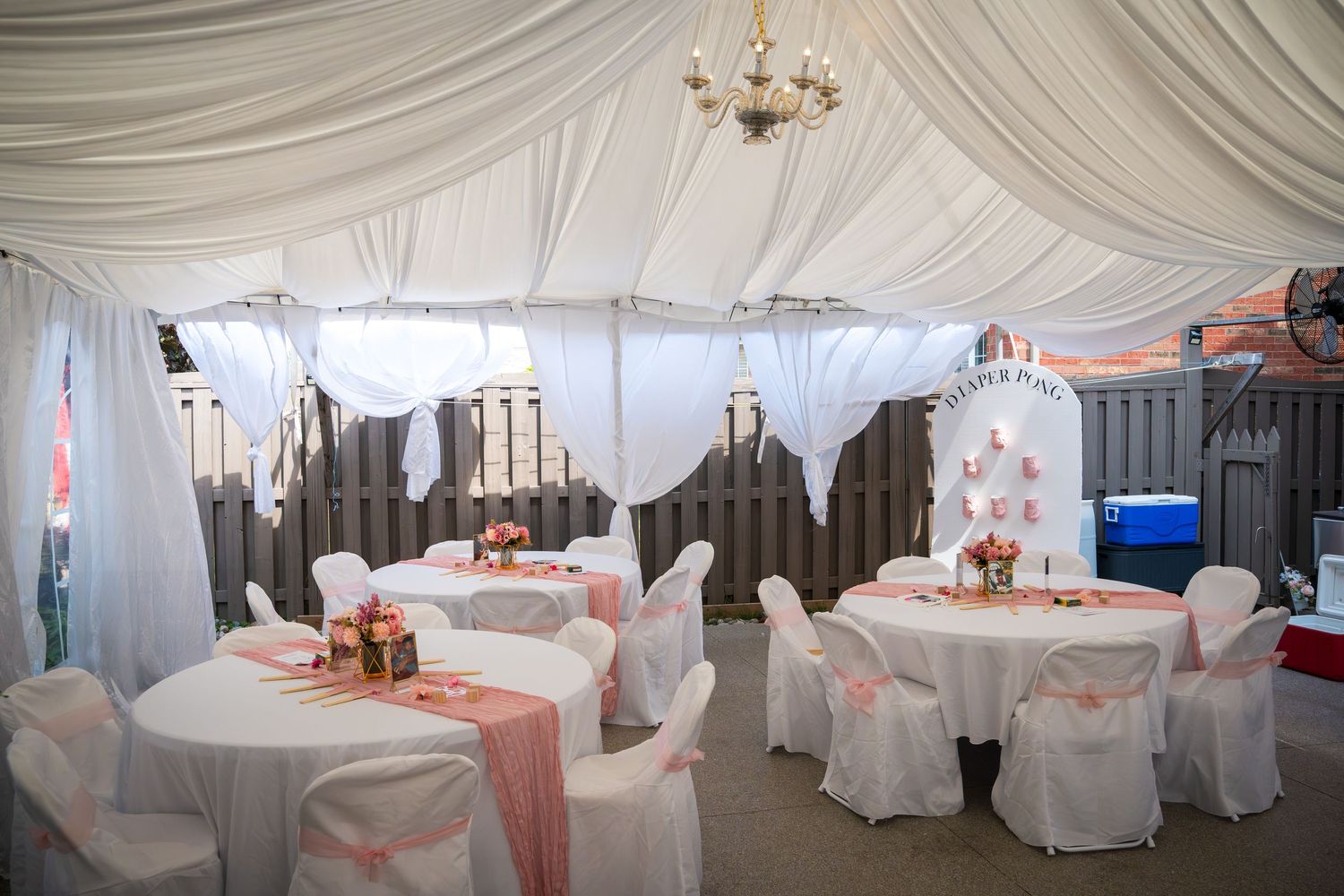 Wide angle view of a white draped wedding tent with chandelier and table settings.
