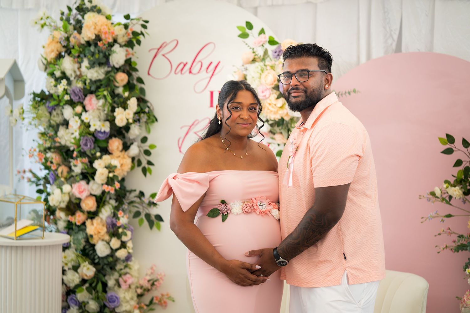 A couple celebrates a special moment in front of an elegant floral wall with pink accents.
