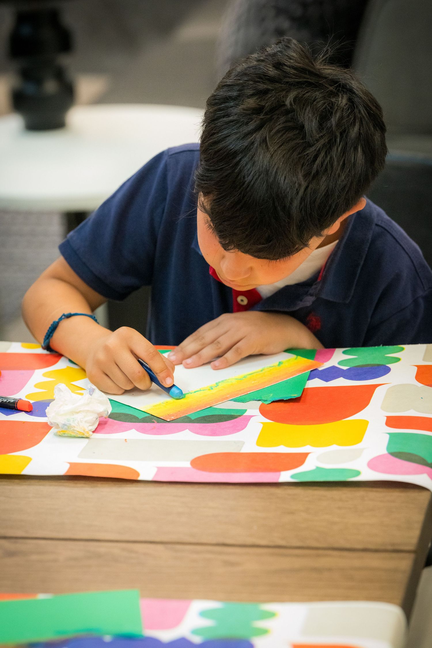 Young boy using a ruler to draw on white paper at a colorful craft table.