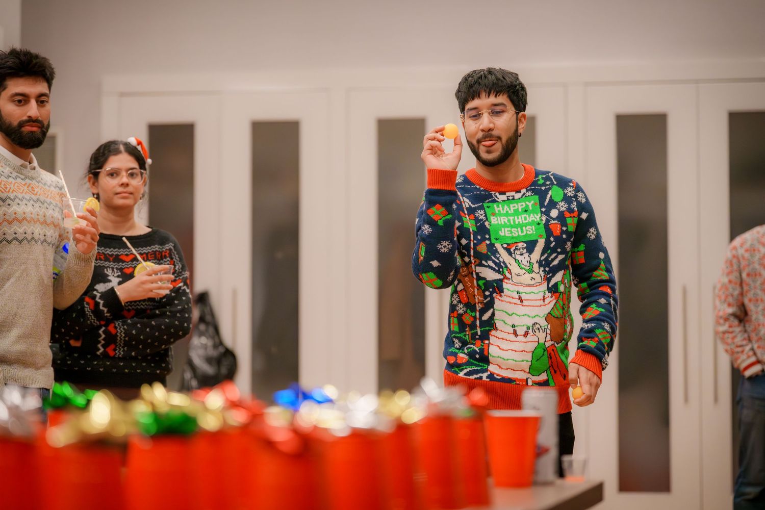 Group wearing holiday sweaters posing near red cups at a party.
