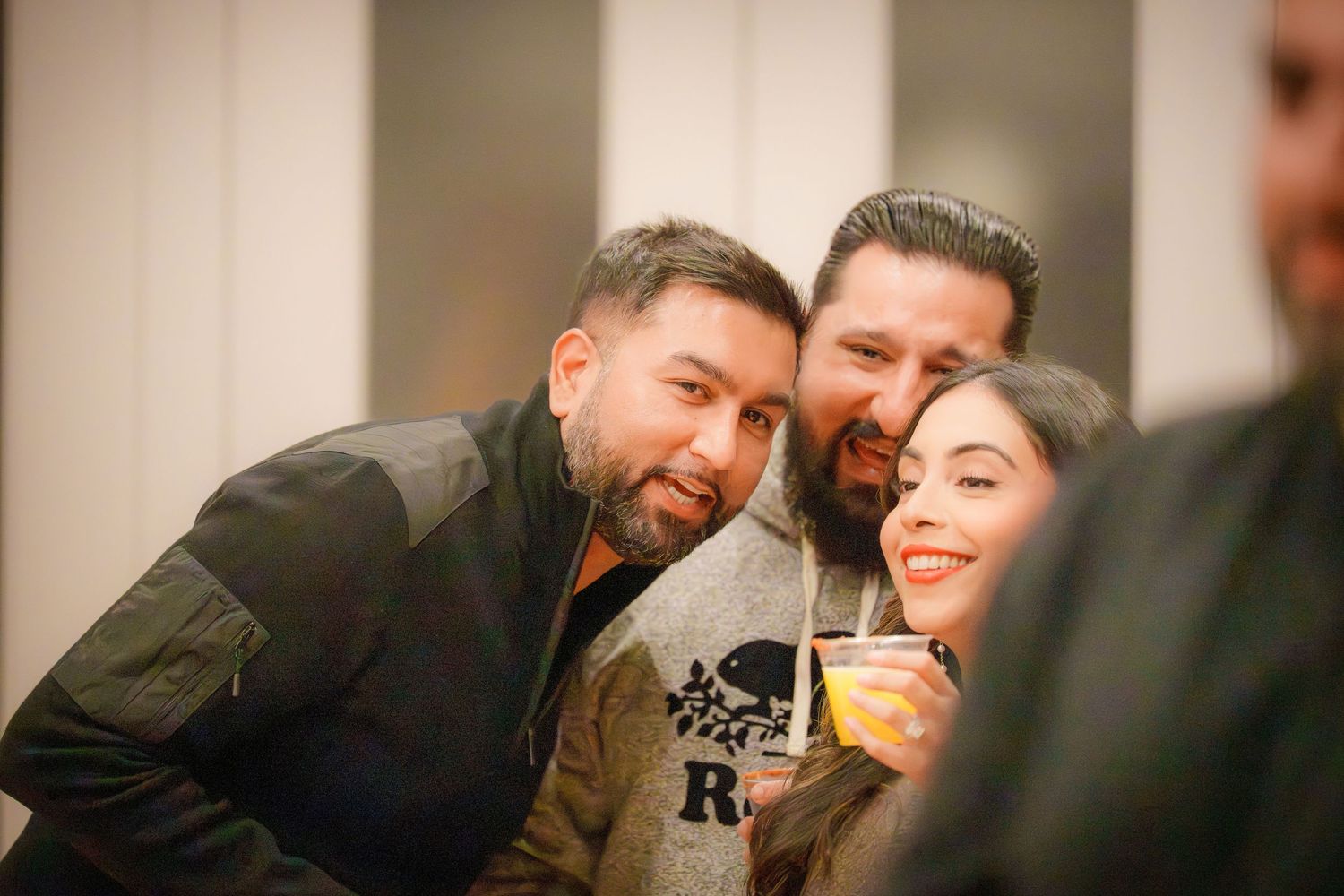 Friends laughing and socializing at an indoor party with drinks and festive atmosphere.