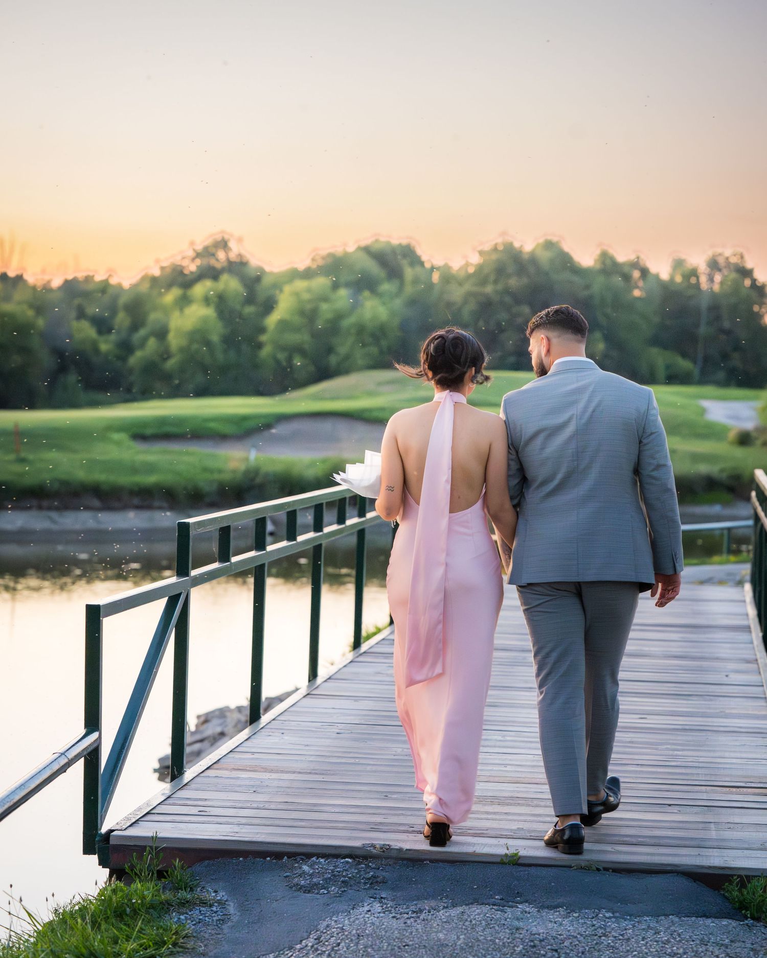 A couple walking together on a wooden boardwalk overlooking a lake at sunset.