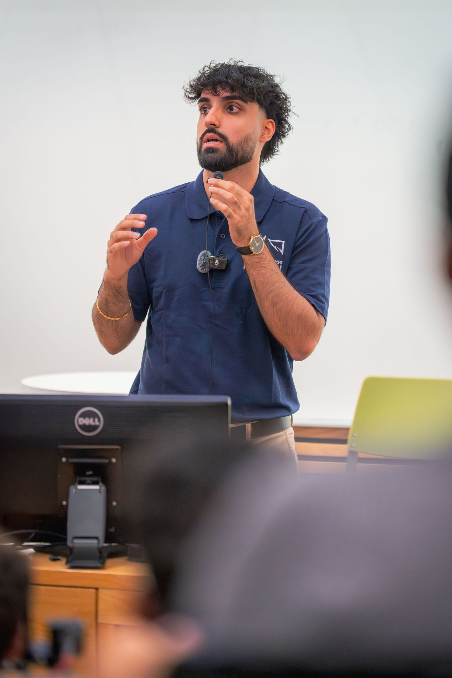 Speaker gesturing while giving a presentation in a navy polo shirt.