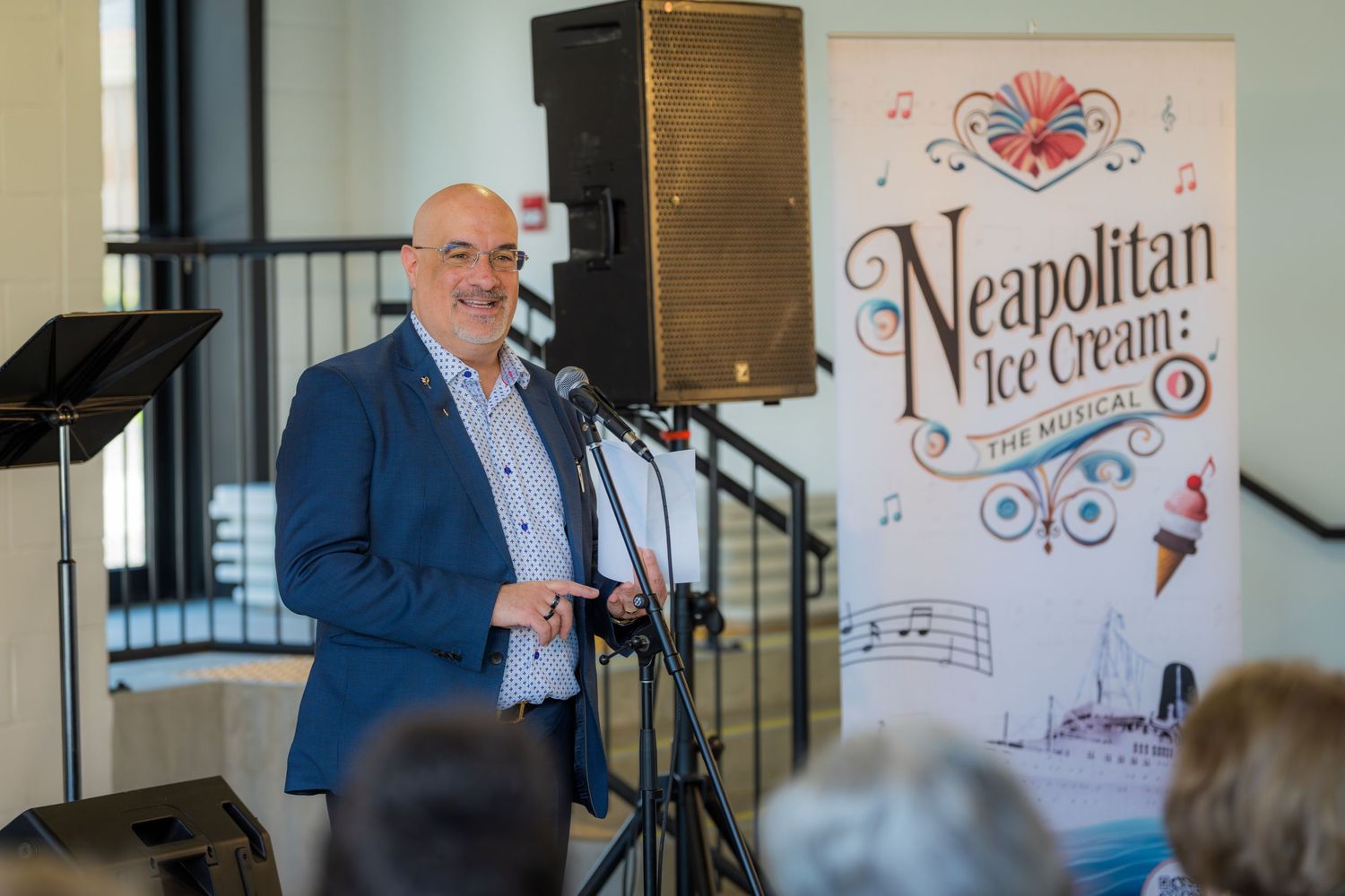 Man speaking at microphone podium at Neapolitan Ice Cream The Musical promotional event.