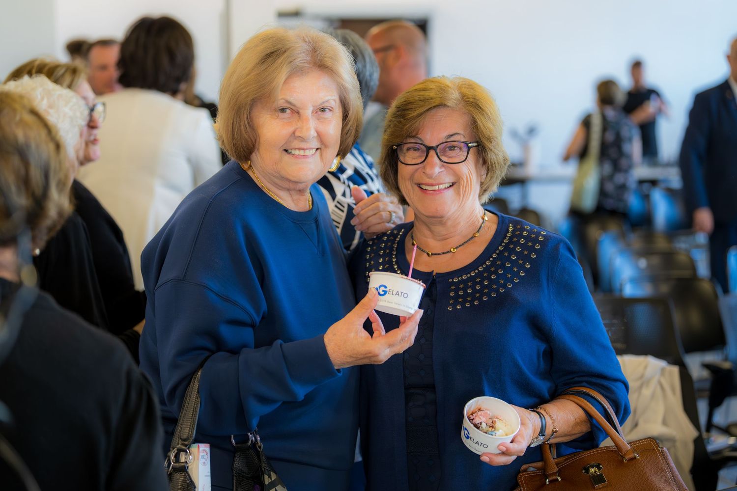 Two smiling women in navy sweaters holding ice cream cups at a Neapolitan Ice Cream Musical event.