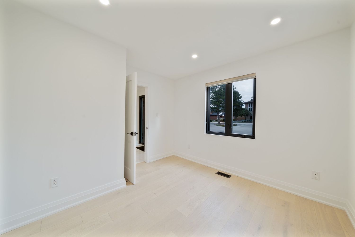Modern white hallway with recessed lighting, hardwood floors, and a small window at the end.
