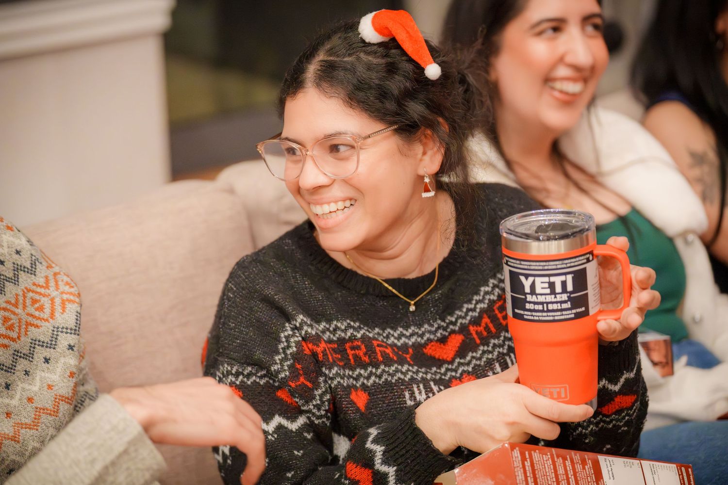 Holiday party attendees in festive sweaters holding drinks and snacks.