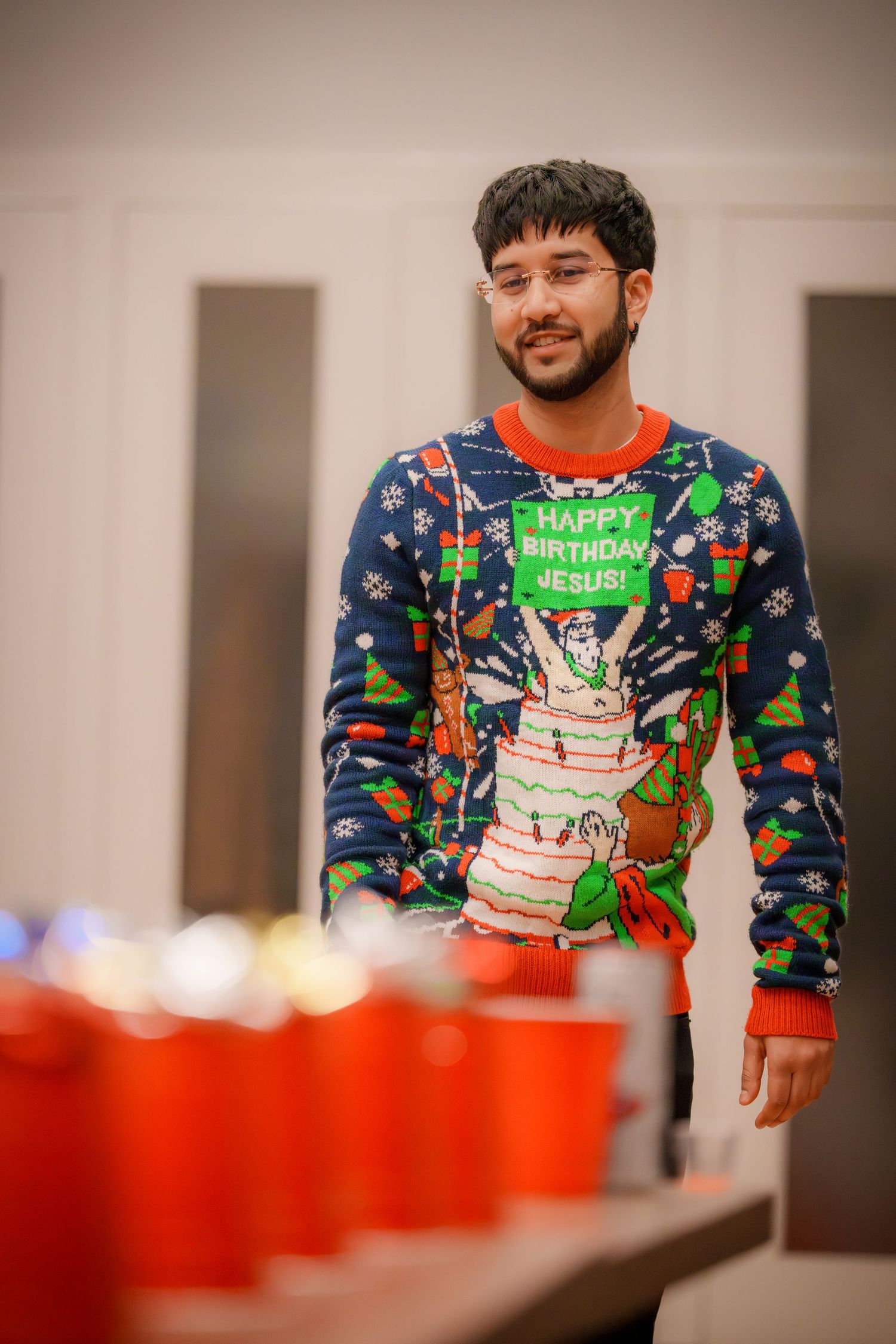 Person wearing a festive blue and red Happy Birthday sweater stands near red party cups at a celebration.