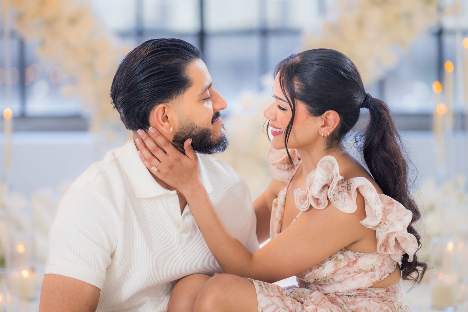 Joyful couple laughing and looking at each other during a romantic engagement photoshoot with white flowers.