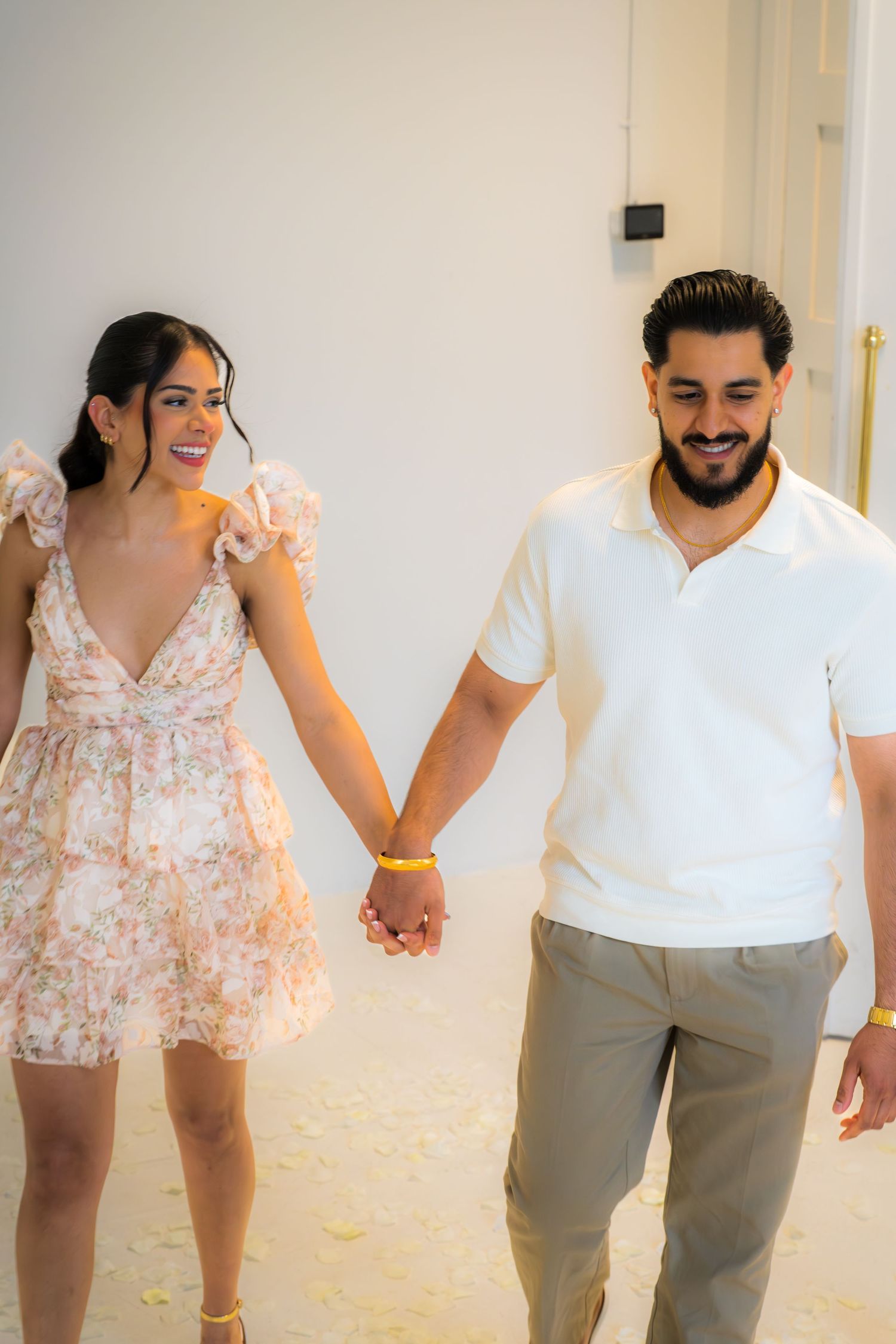 Happy couple walking hand in hand through a flower-petal-covered floor in a romantic proposal venue.