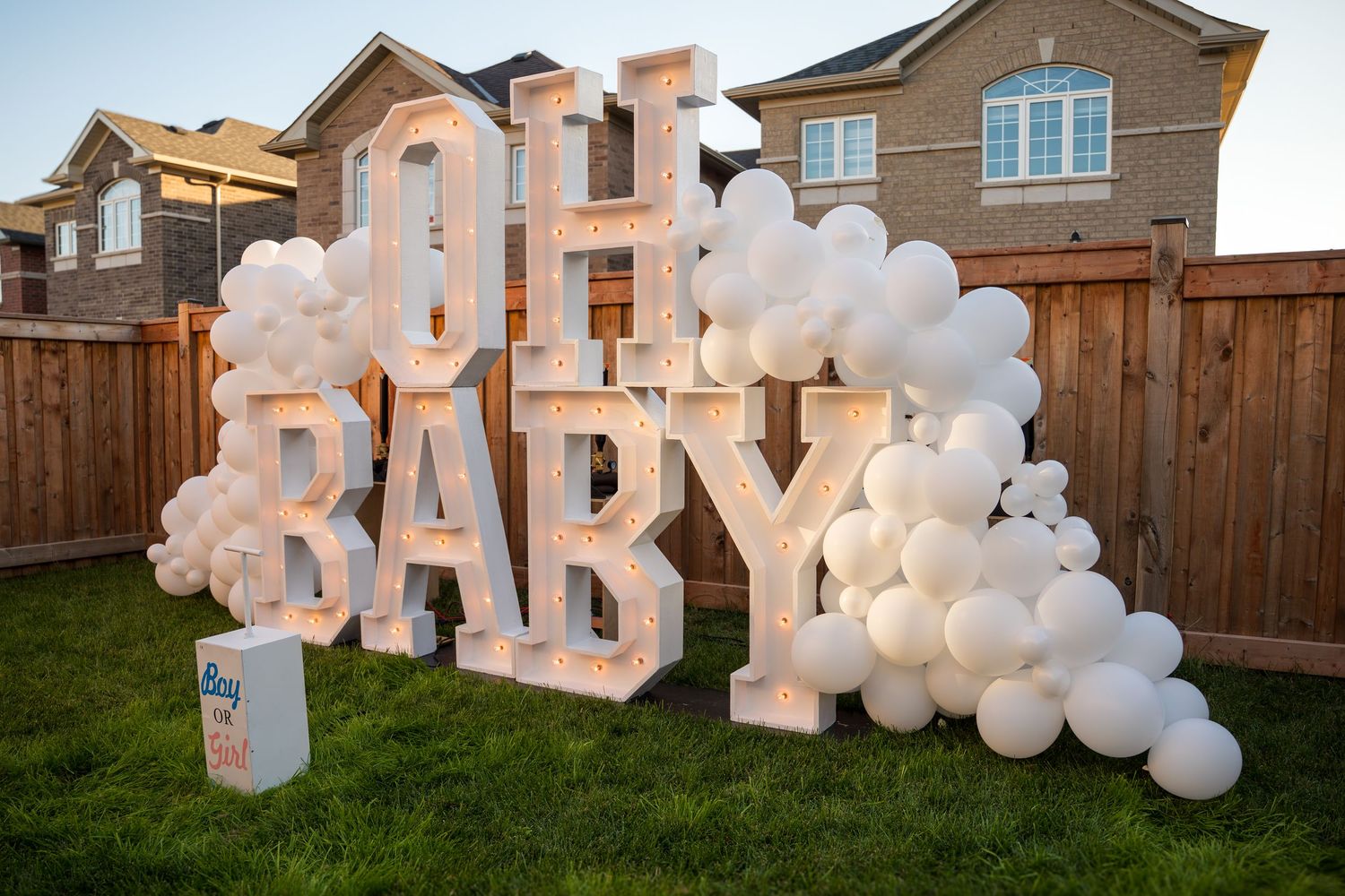 Illuminated OH BABY marquee letters with white balloon garland and Boy or Girl sign at outdoor gender reveal.