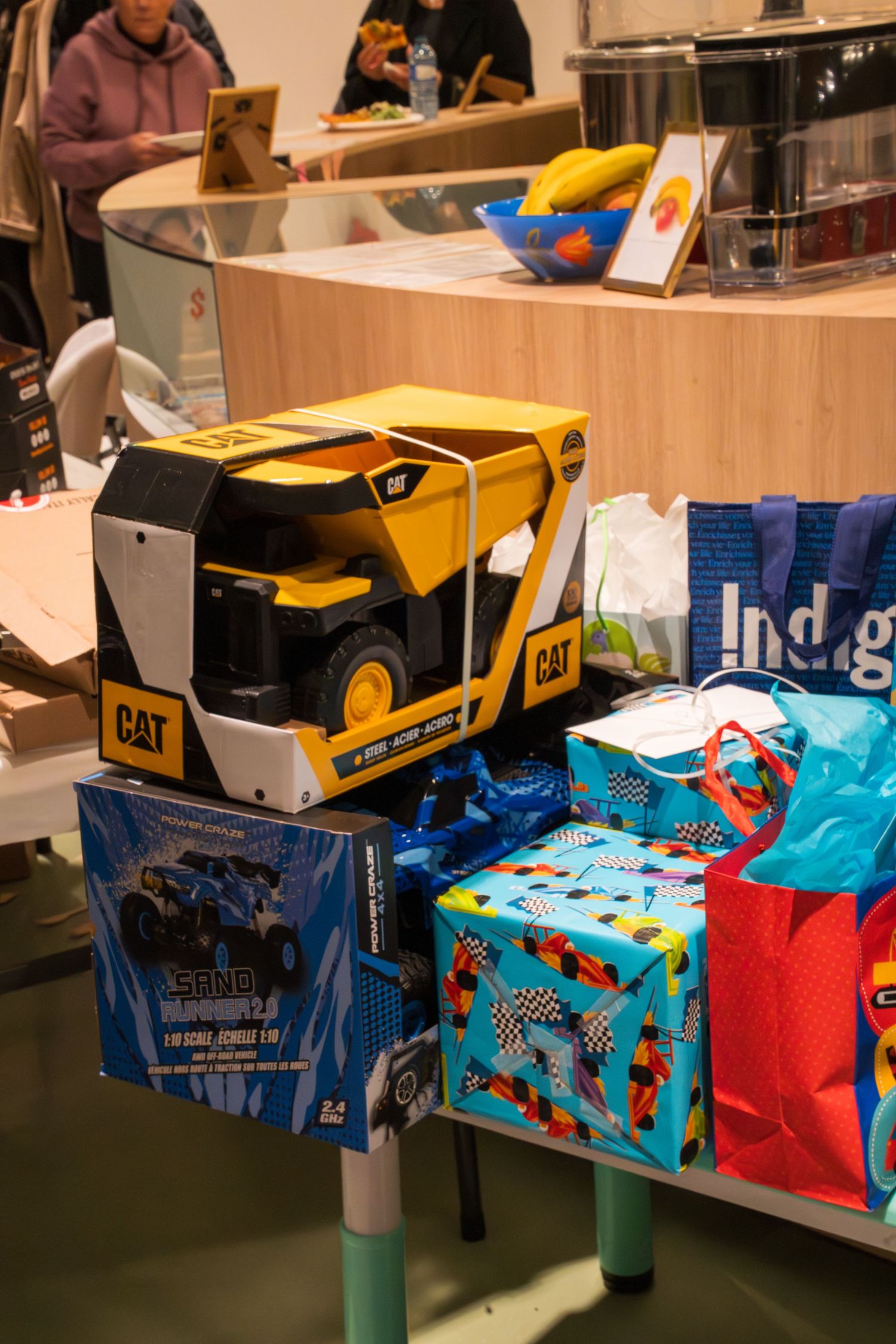 CAT yellow dump truck toy in box displayed on table with colorful birthday gifts and gift bags at a party.