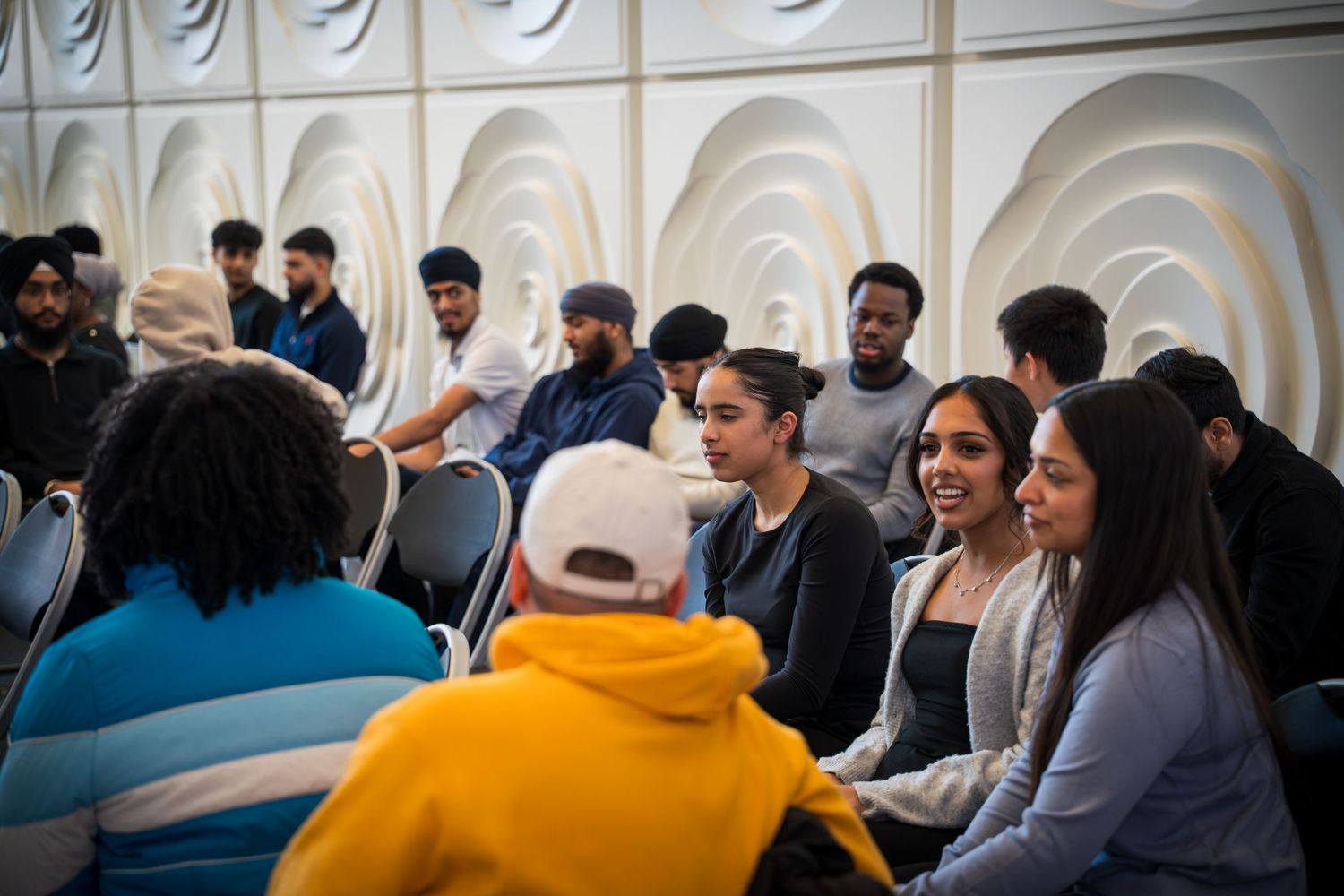 Diverse group of attendees seated in rows at a professional event with textured white wall panels.