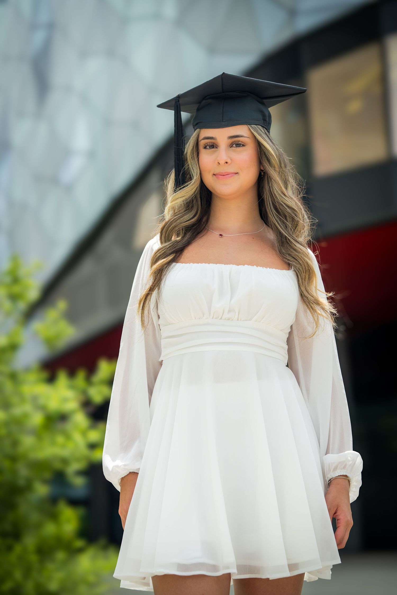 Graduation photo session showing white dress and mortarboard cap against modern backdrop.
