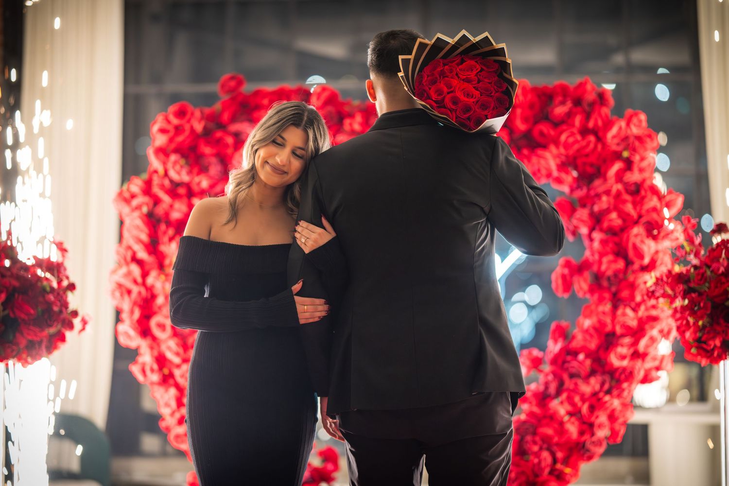 Romantic proposal setup with red floral arch and ambient lighting creating an intimate atmosphere.