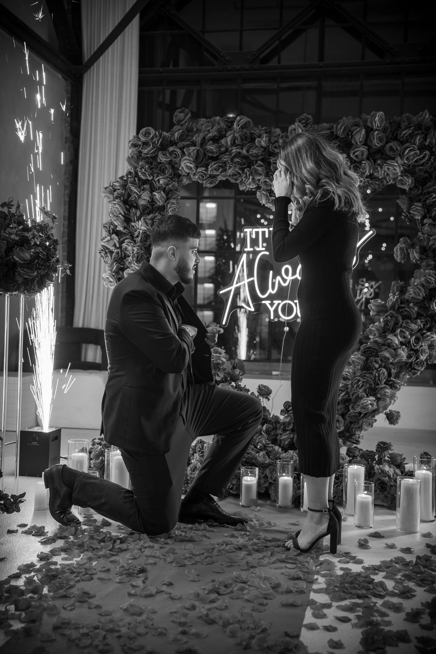 Candlelit proposal scene with scattered rose petals and illuminated signage.