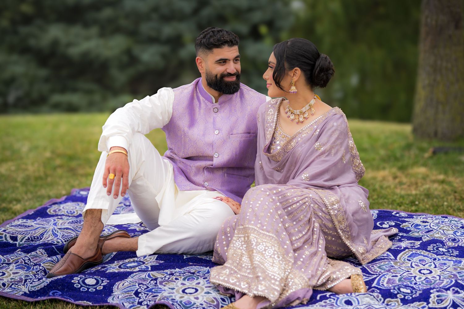 Couple relaxing on blue patterned blanket during outdoor photoshoot in park setting.
