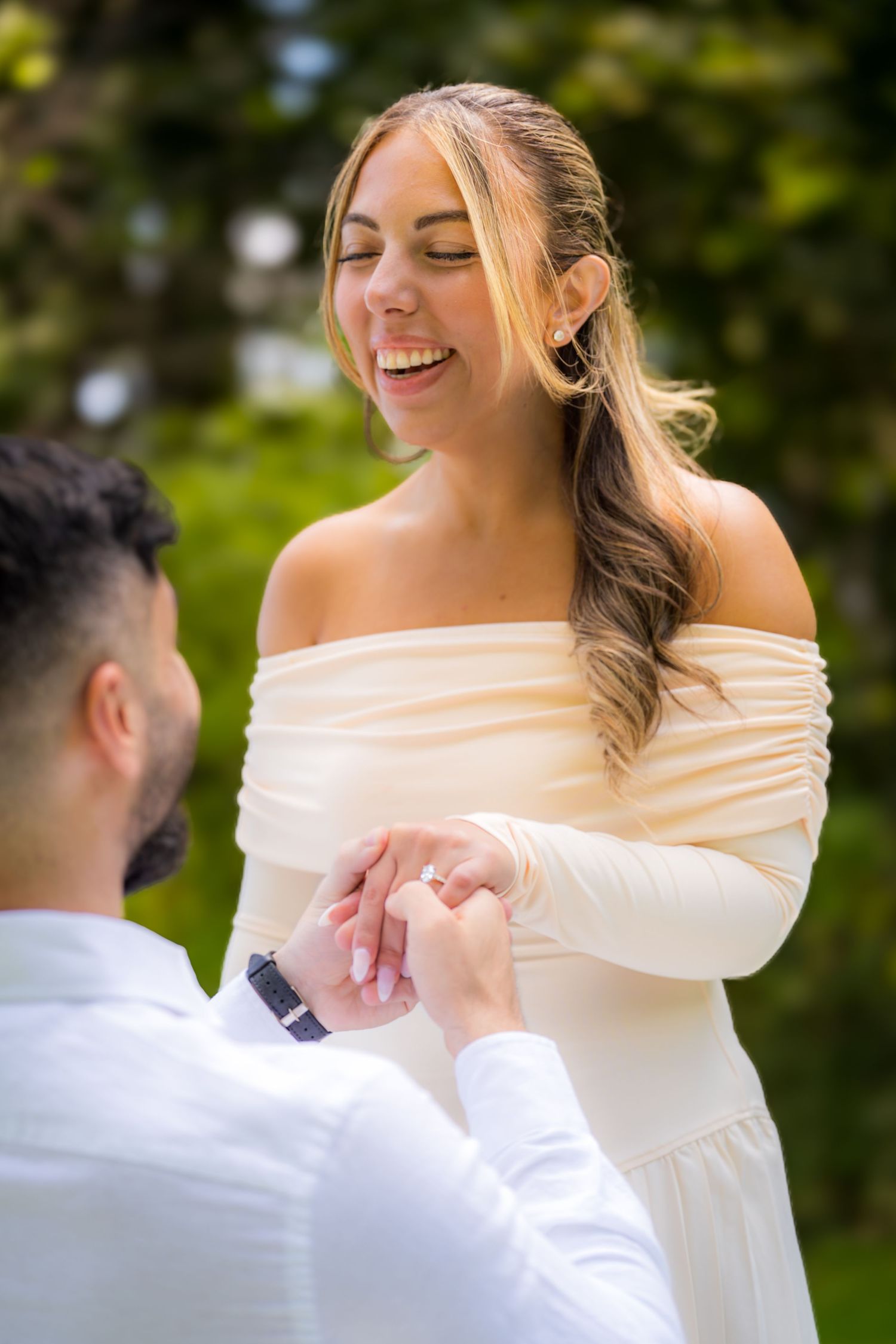 A joyful moment during a surprise proposal with white floral decorations in the background.
